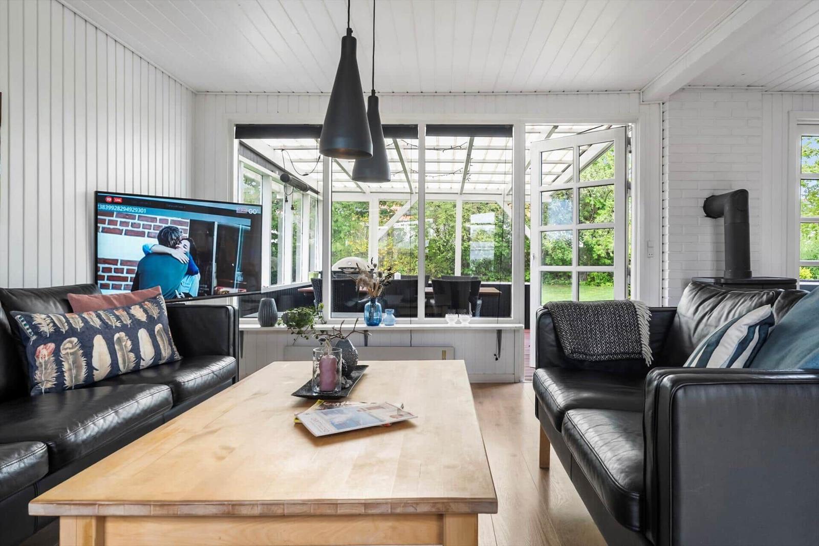 Wohnzimmer mit zwei schwarzen Sofas, Holztisch und TV. Durchgang zu Terrasse mit Gartenblick.