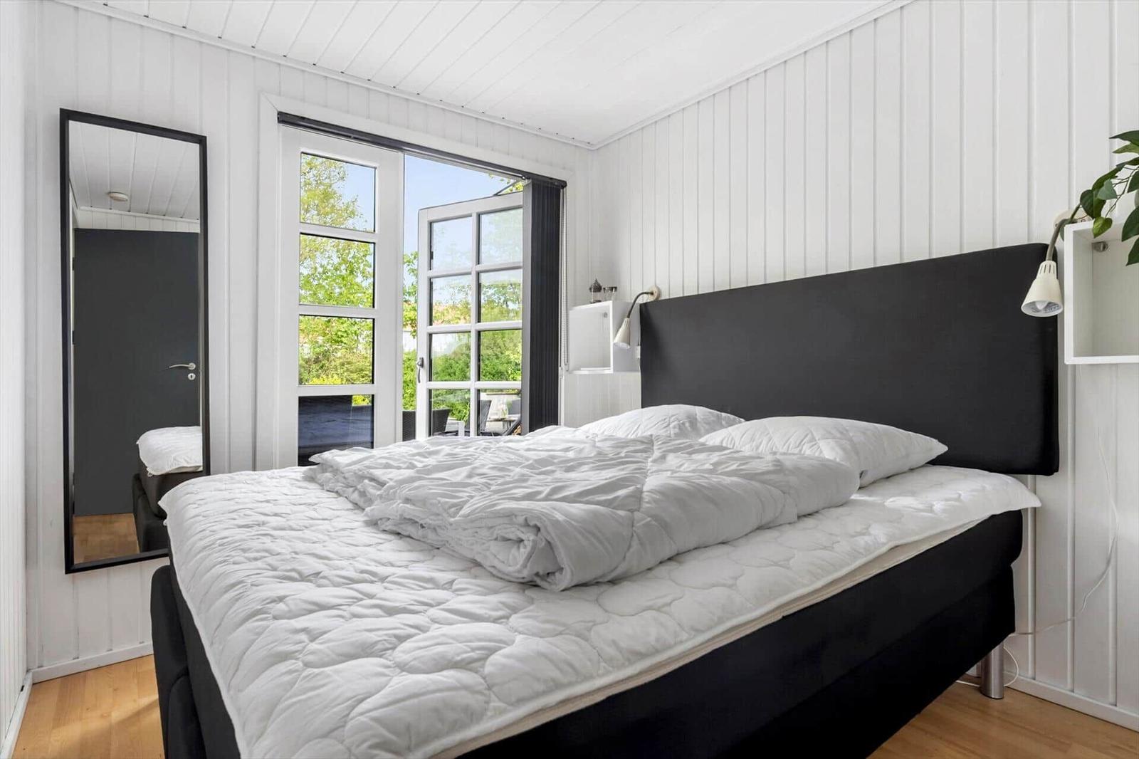 Schlafzimmer mit weißem Bett, Fenster und Spiegel an der Wand.