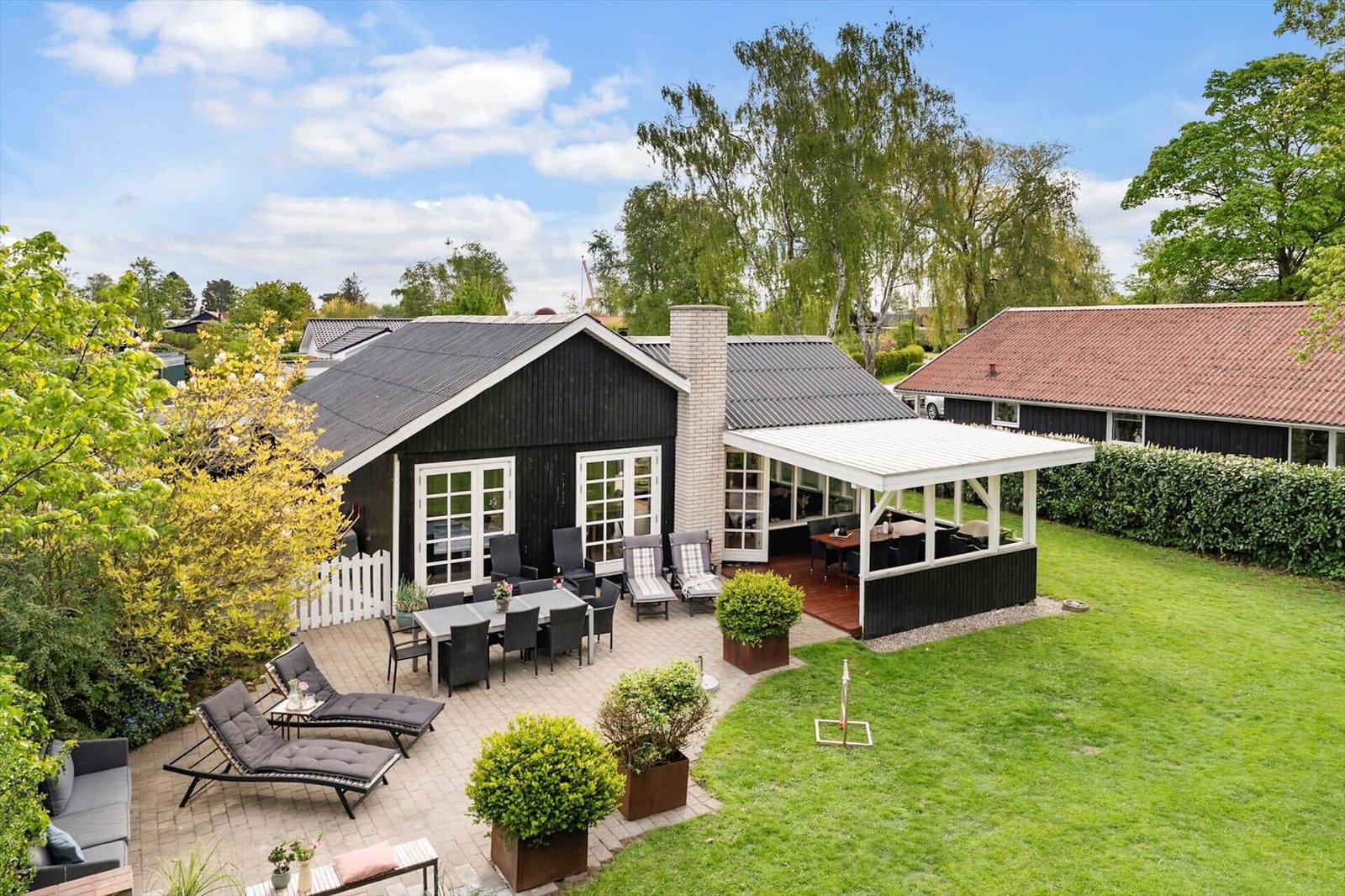 Schwarzes Haus mit Terrasse, Garten und Pavillon. Möblierte Außengestaltung.