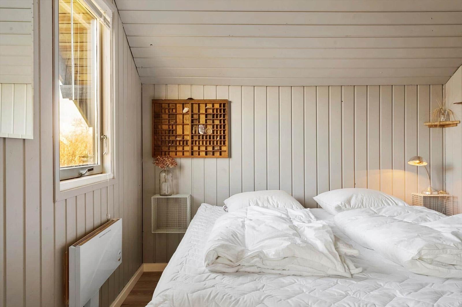 Schlafzimmer mit weißem Bett, Holzwand und Fenster.