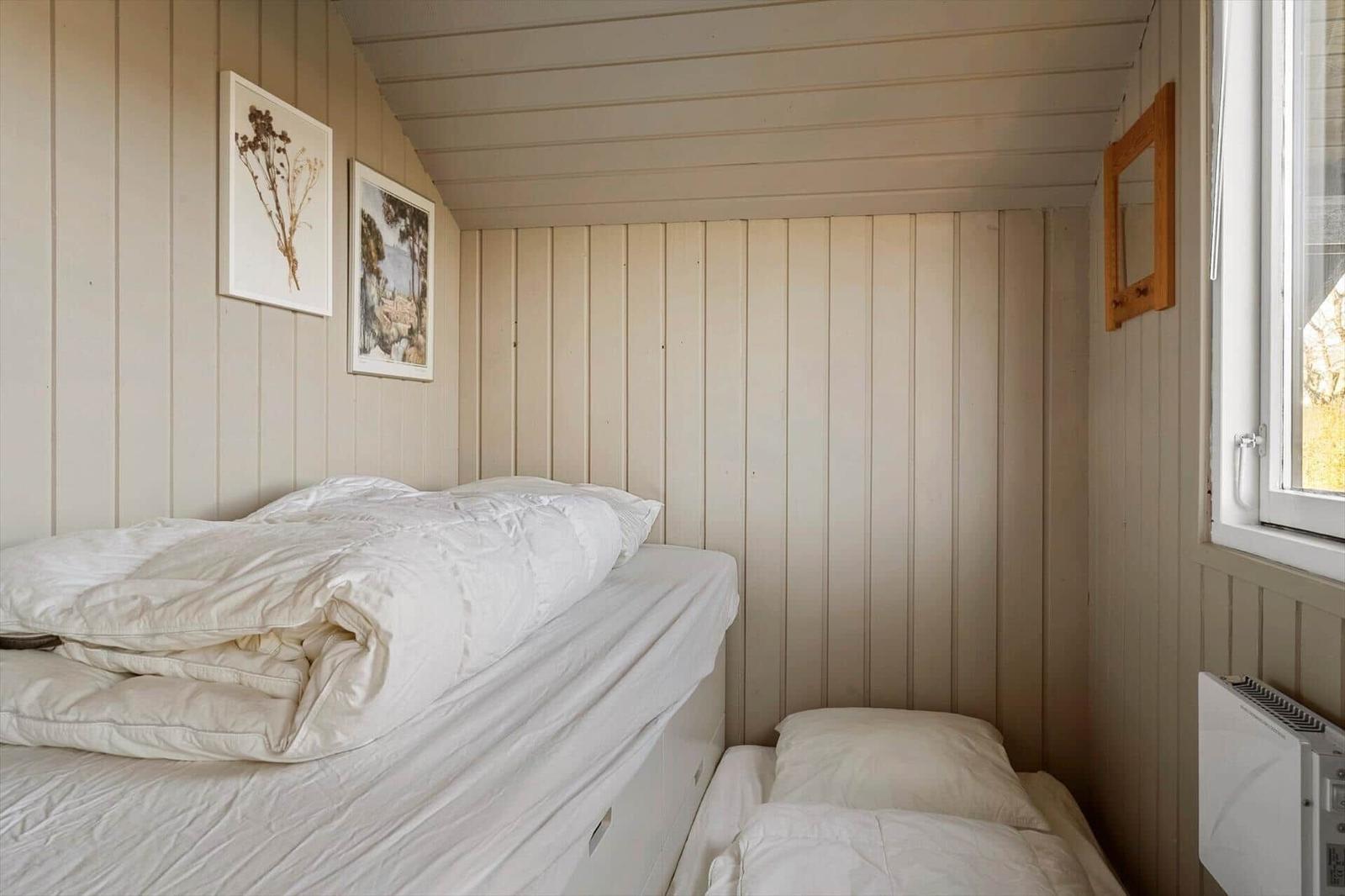 Schlafzimmer mit zwei Betten, Holzwänden und Fenster. Wandbilder und Spiegel hängen an den Wänden.