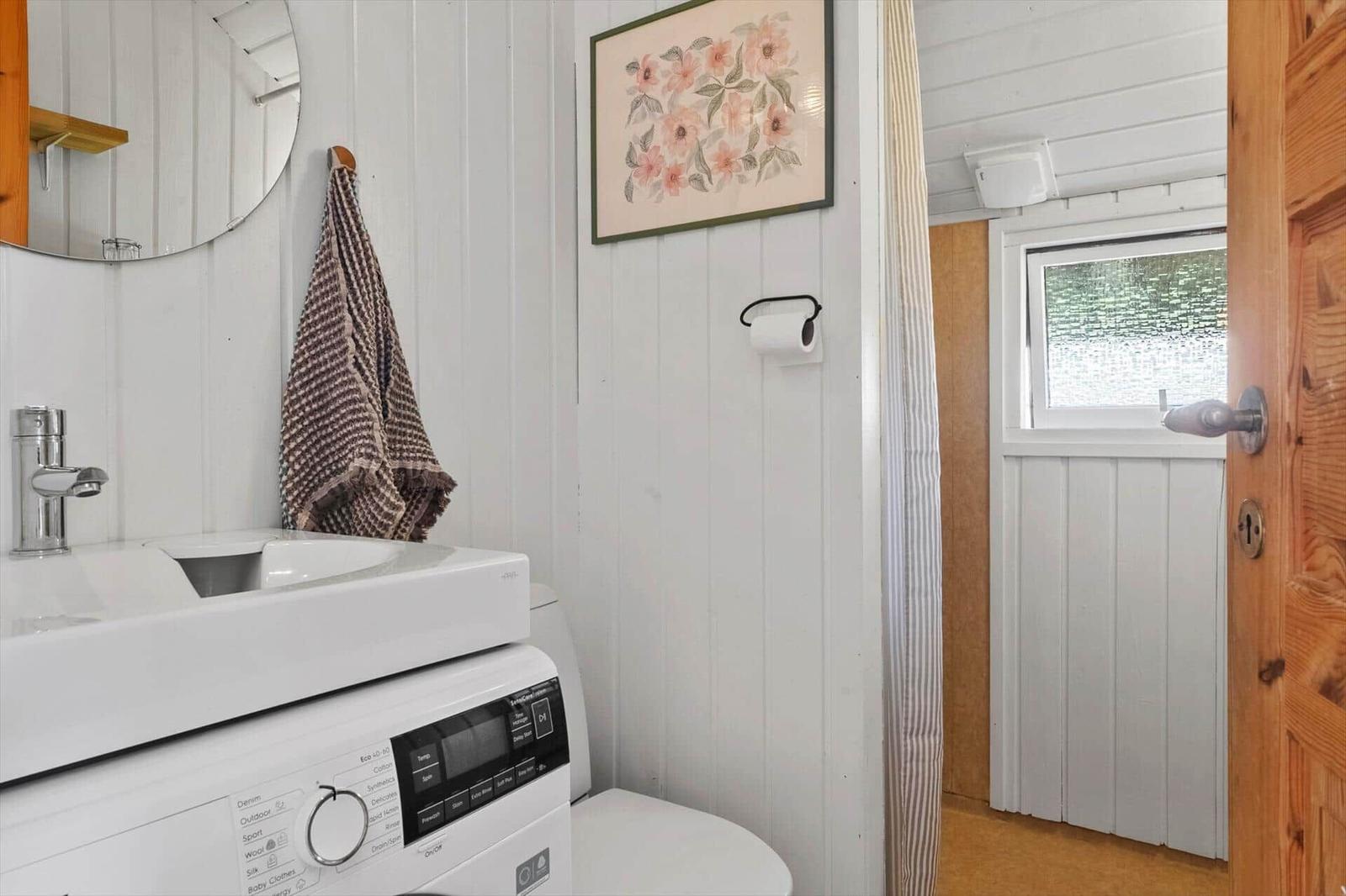 Badezimmer mit Waschmaschine, Spiegel und Fenster. Holztür und Wandverkleidung.