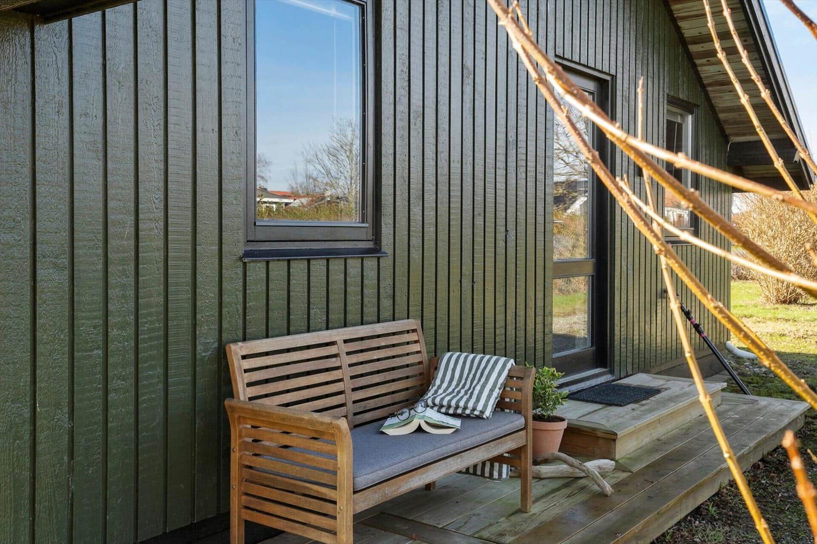 Holzbank mit Kissen und Buch vor grünem Holzhaus mit Fenster und Tür.