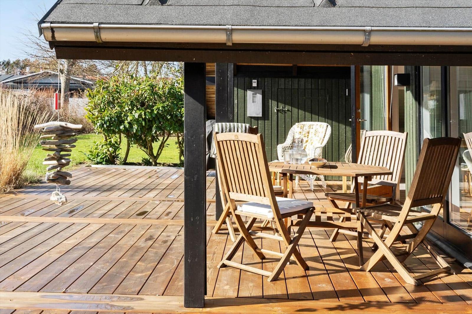 Terrasse mit Holztisch und Stühlen unter Dach, Blick auf Garten und Haus.