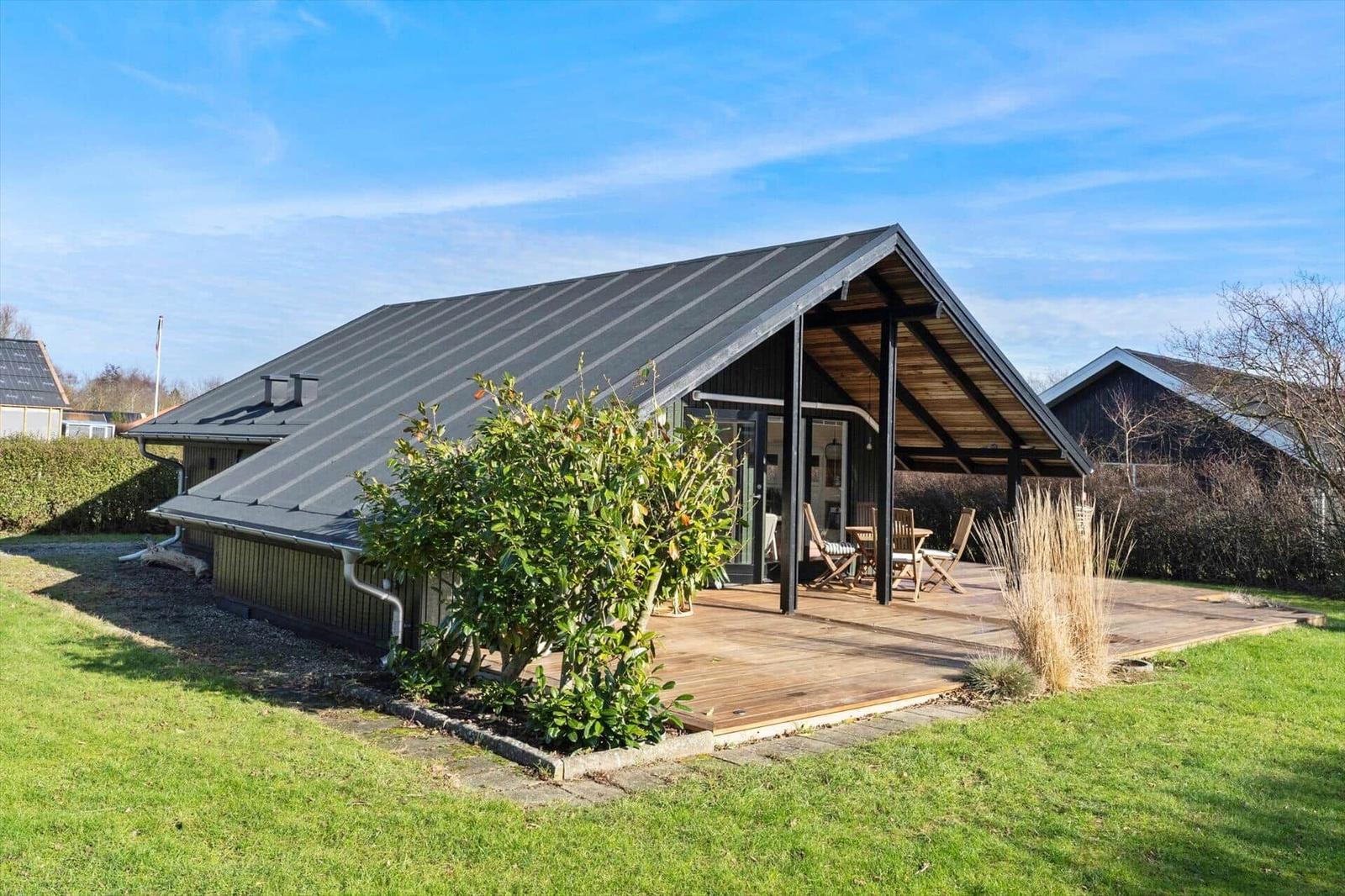 Moderne Hütte mit Holzterrasse und Garten. Sicht auf Terrasse mit Stühlen und Tisch.