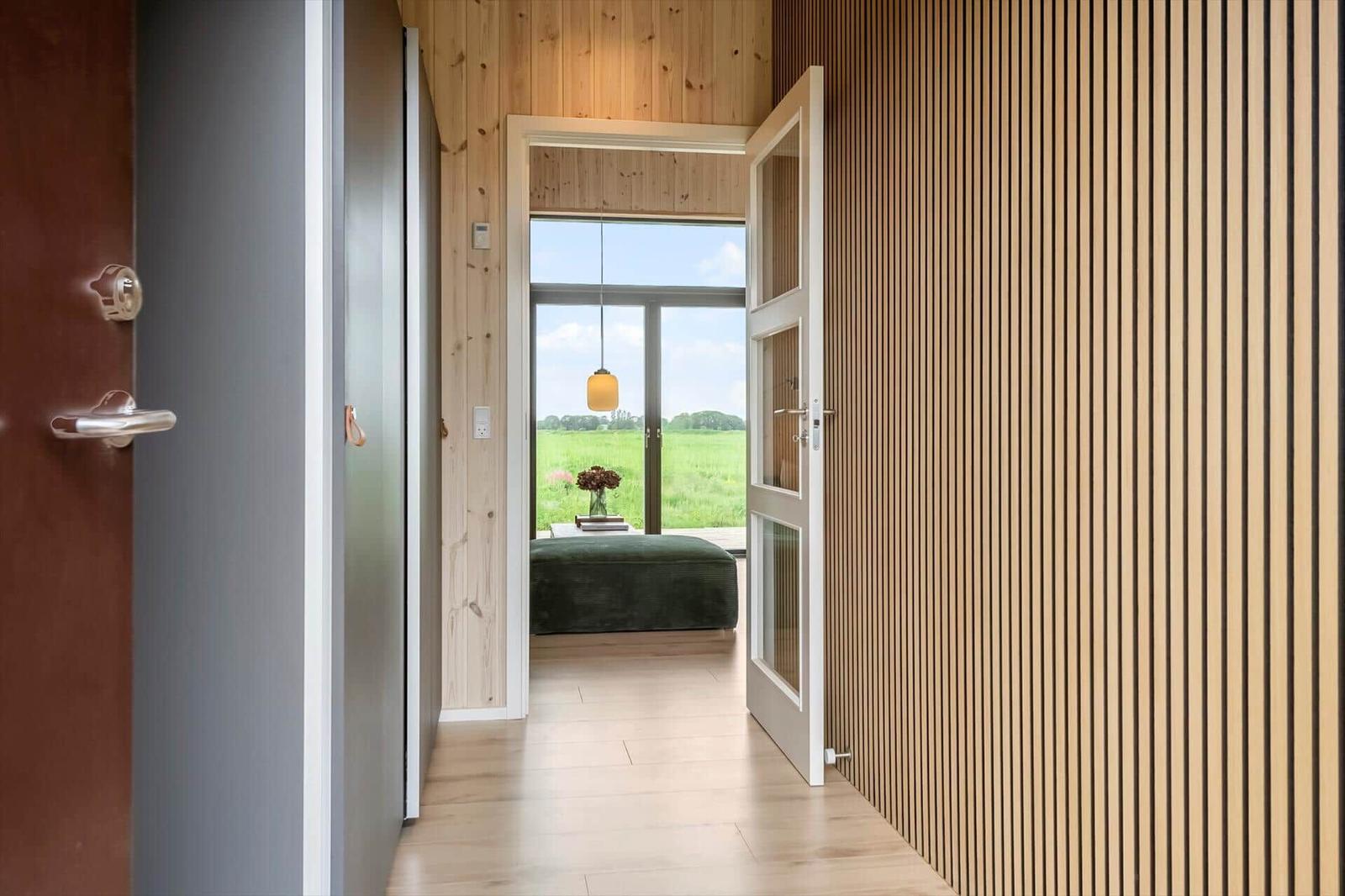 Durchgang mit Holzwand und Tür zu einem Raum mit Blick auf grünes Feld.