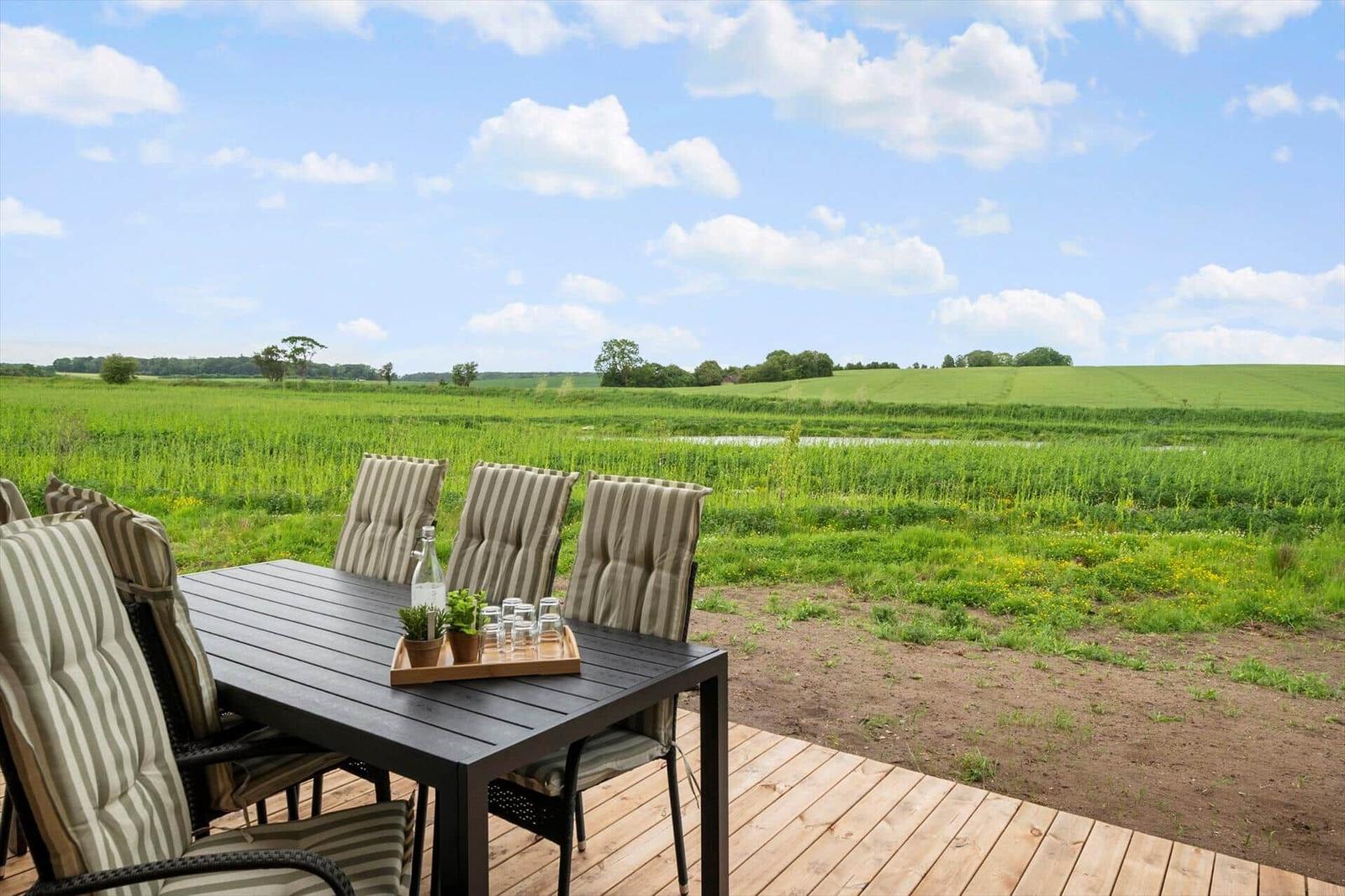 Terrasse mit Tisch und Stühlen. Blick auf grünes Feld und Himmel.