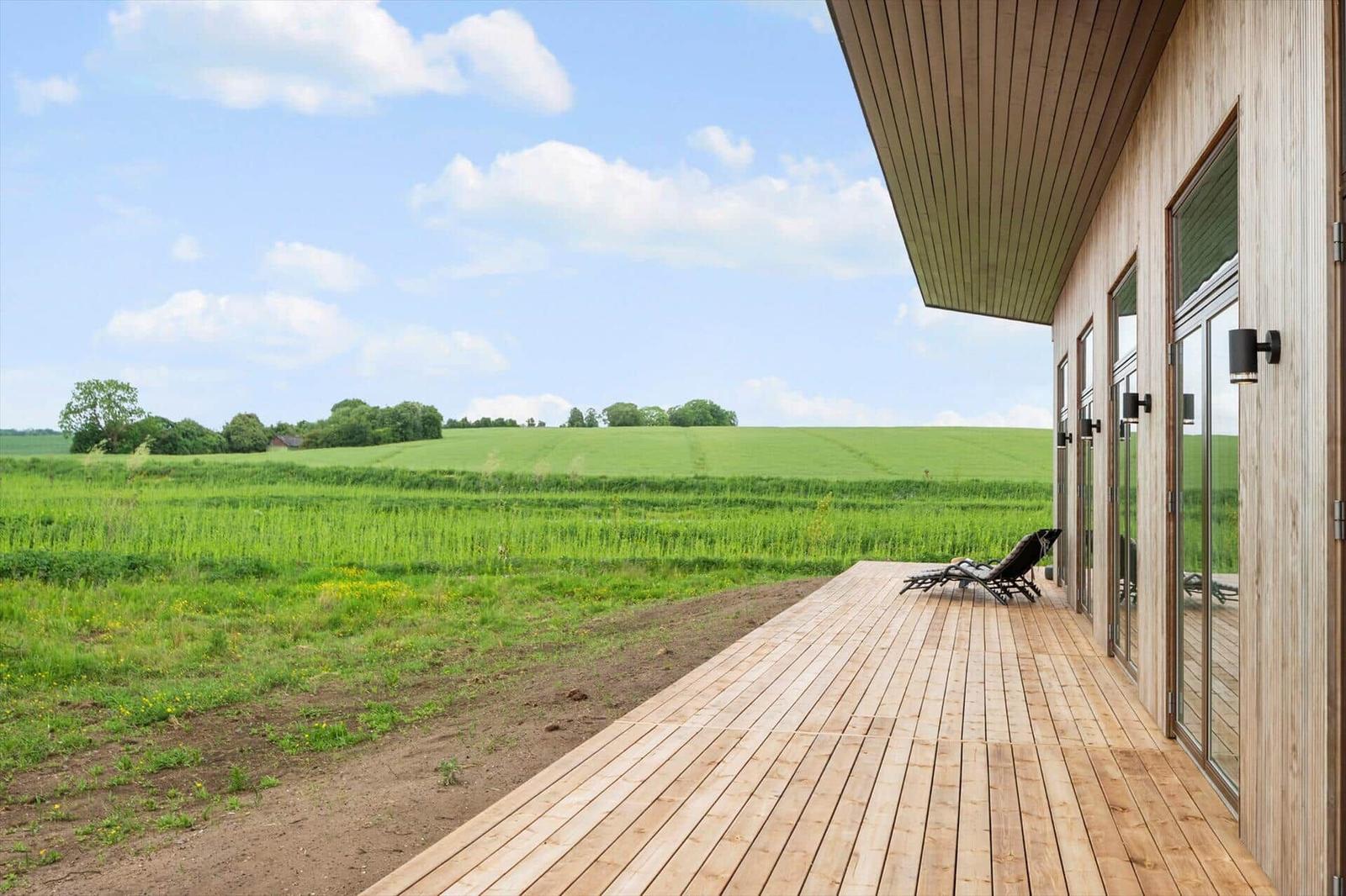 Terrasse mit Liegestuhl und Blick auf grünes Feld unter blauem Himmel.