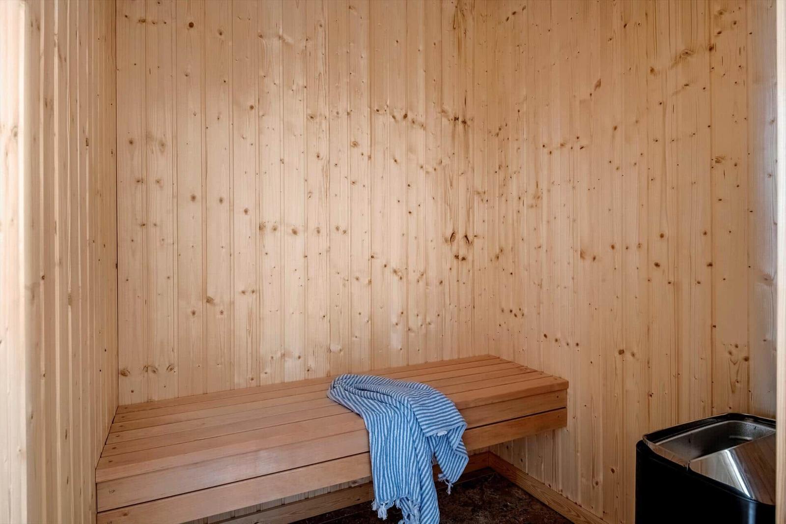 Sauna mit Holzwand und Sitzbank. Ein blau-weiß gestreiftes Handtuch liegt darauf.