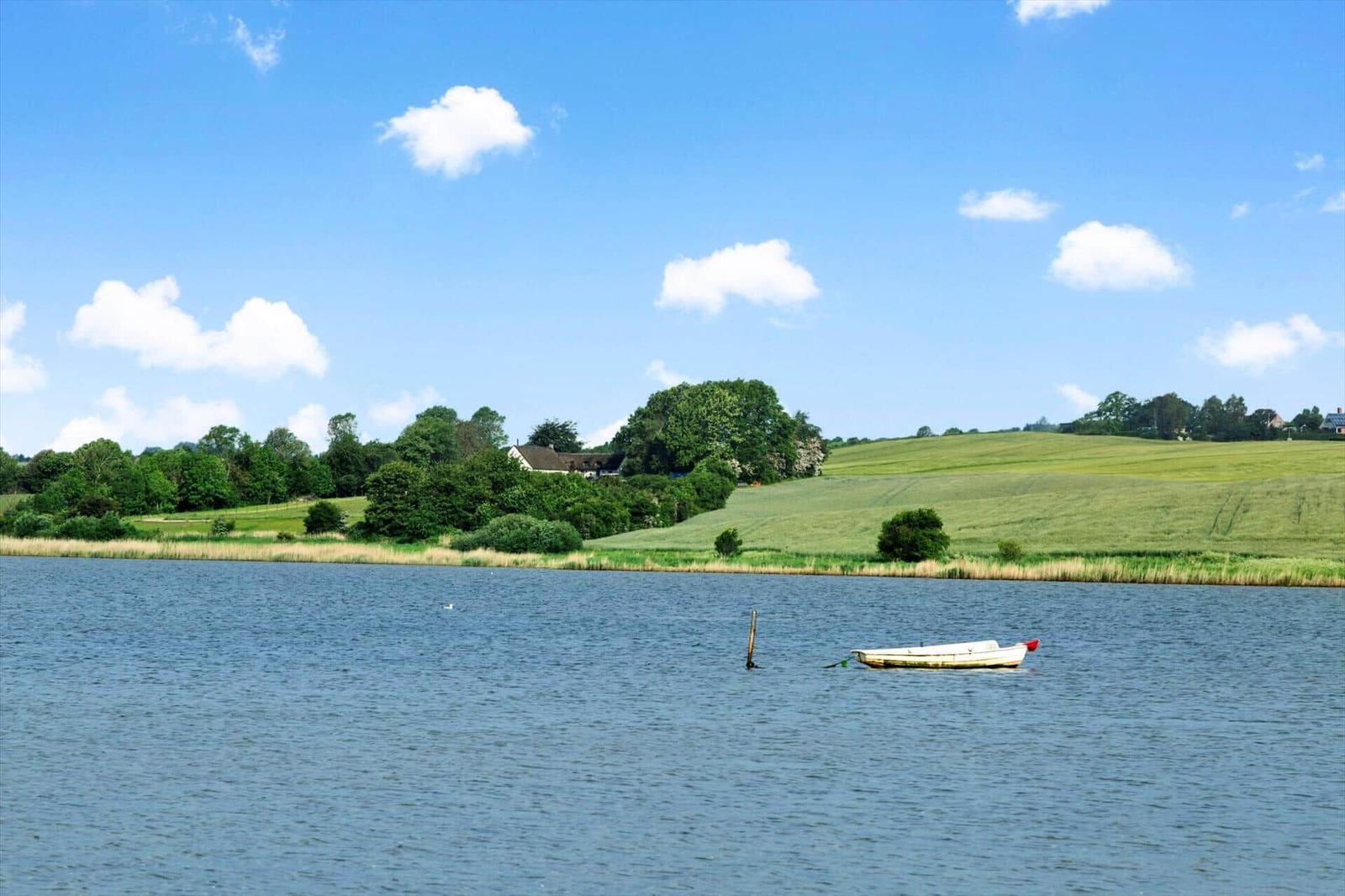 A white boat floats on the lake. Green meadows and trees are visible in the background.