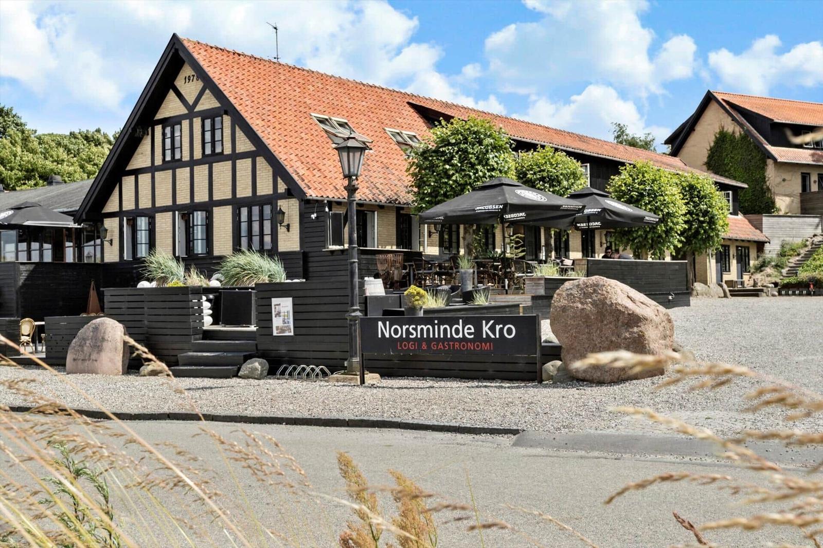 Norsminde Kro with terrace, seating, and stone in foreground.