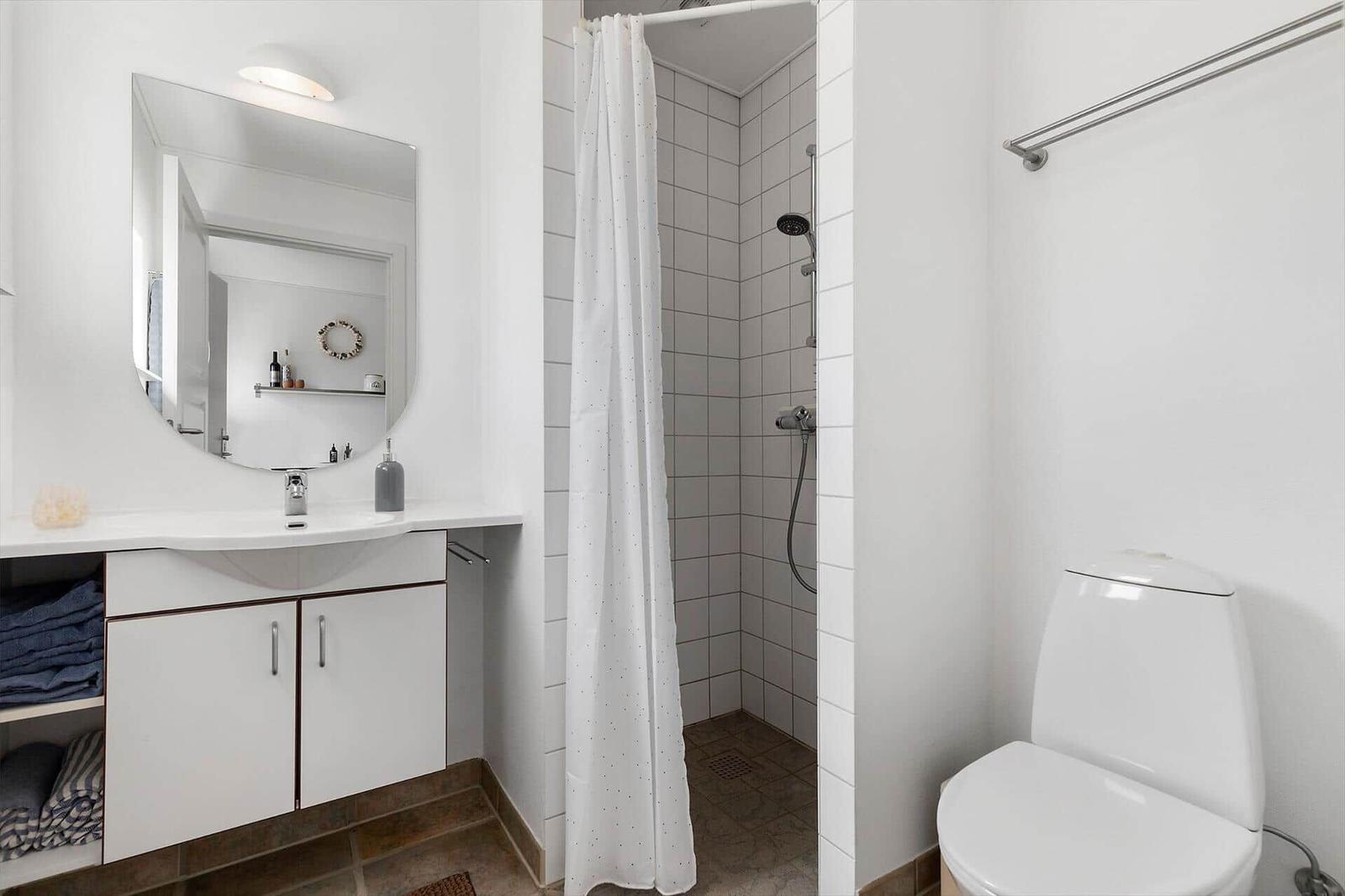 Bathroom with shower, sink, and toilet. White tiles and mirror cabinet.