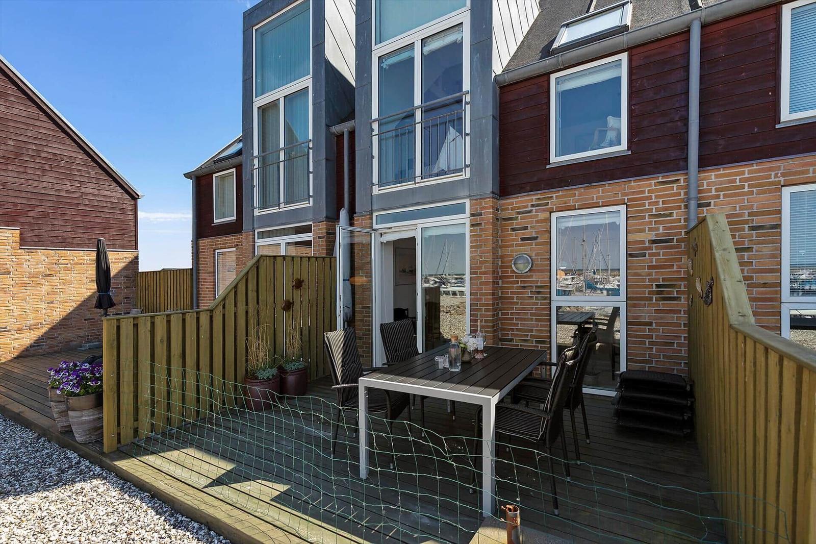 Deck with table, chairs, and harbor view. Wooden railing and plants.