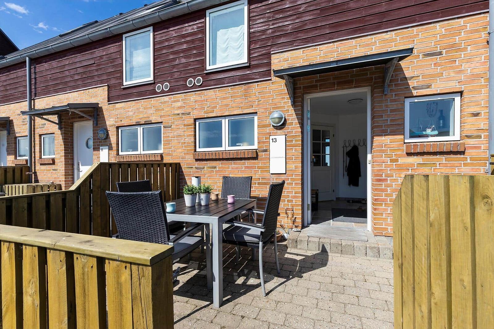 Terrace with table and chairs in front of a house with wooden and brick wall.
