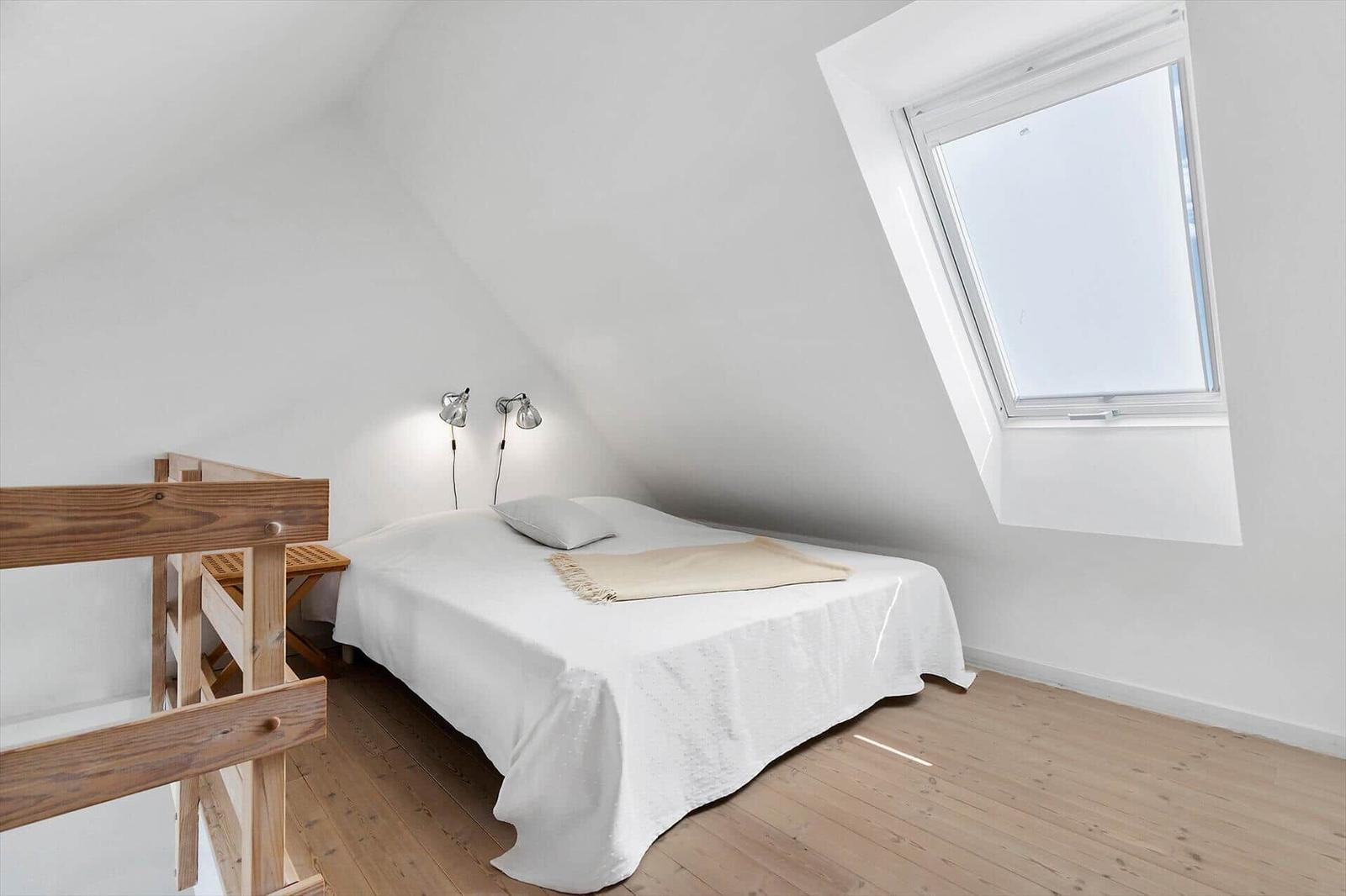 Bedroom with sloped ceiling, bed, window, and wooden floor.