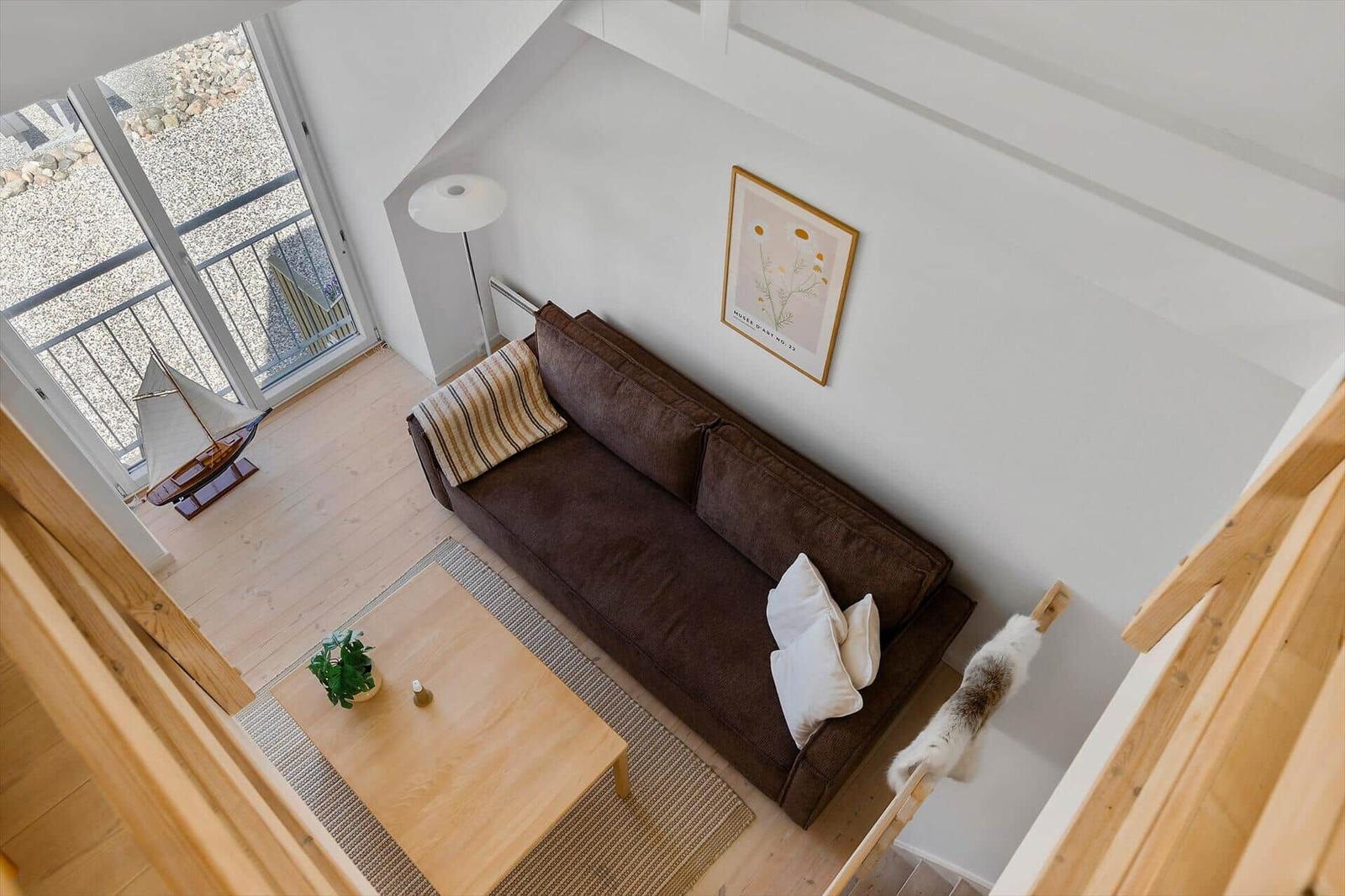 A living room with a brown sofa, wooden table, and window to the terrace.