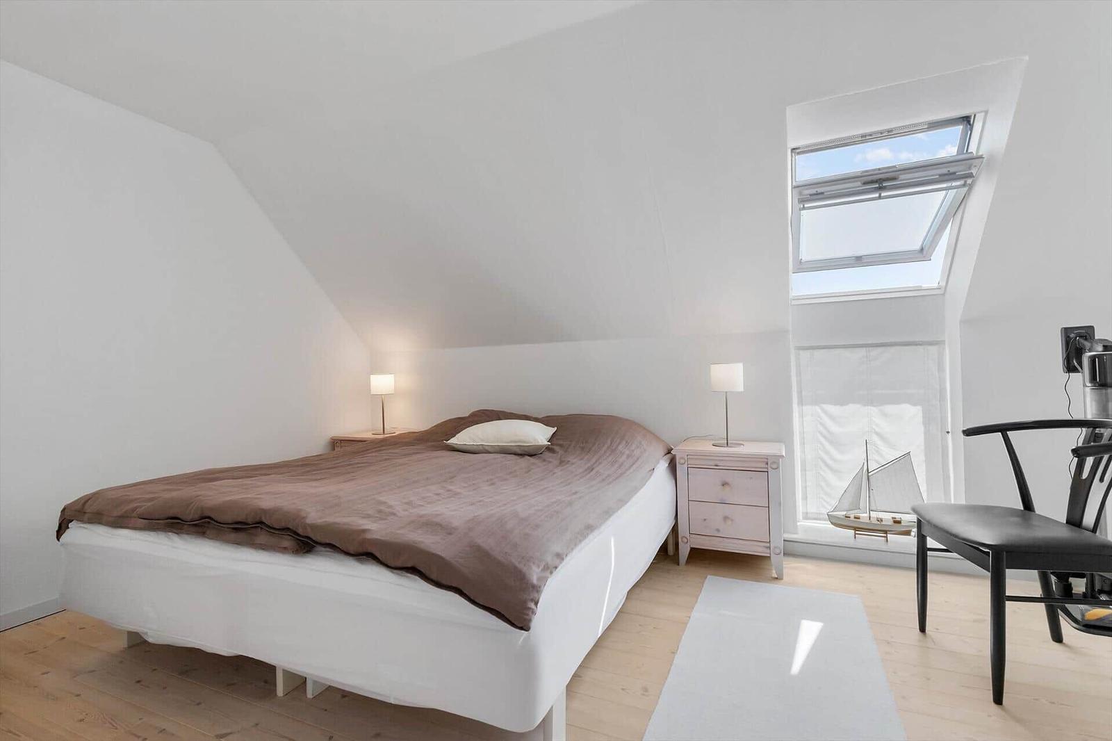 Bedroom with sloped ceiling, bed, nightstand, and skylight.