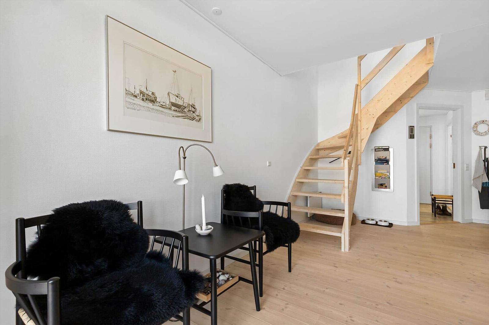 Dining area with table, chairs, and wooden staircase. Wall art and floor lamp visible.