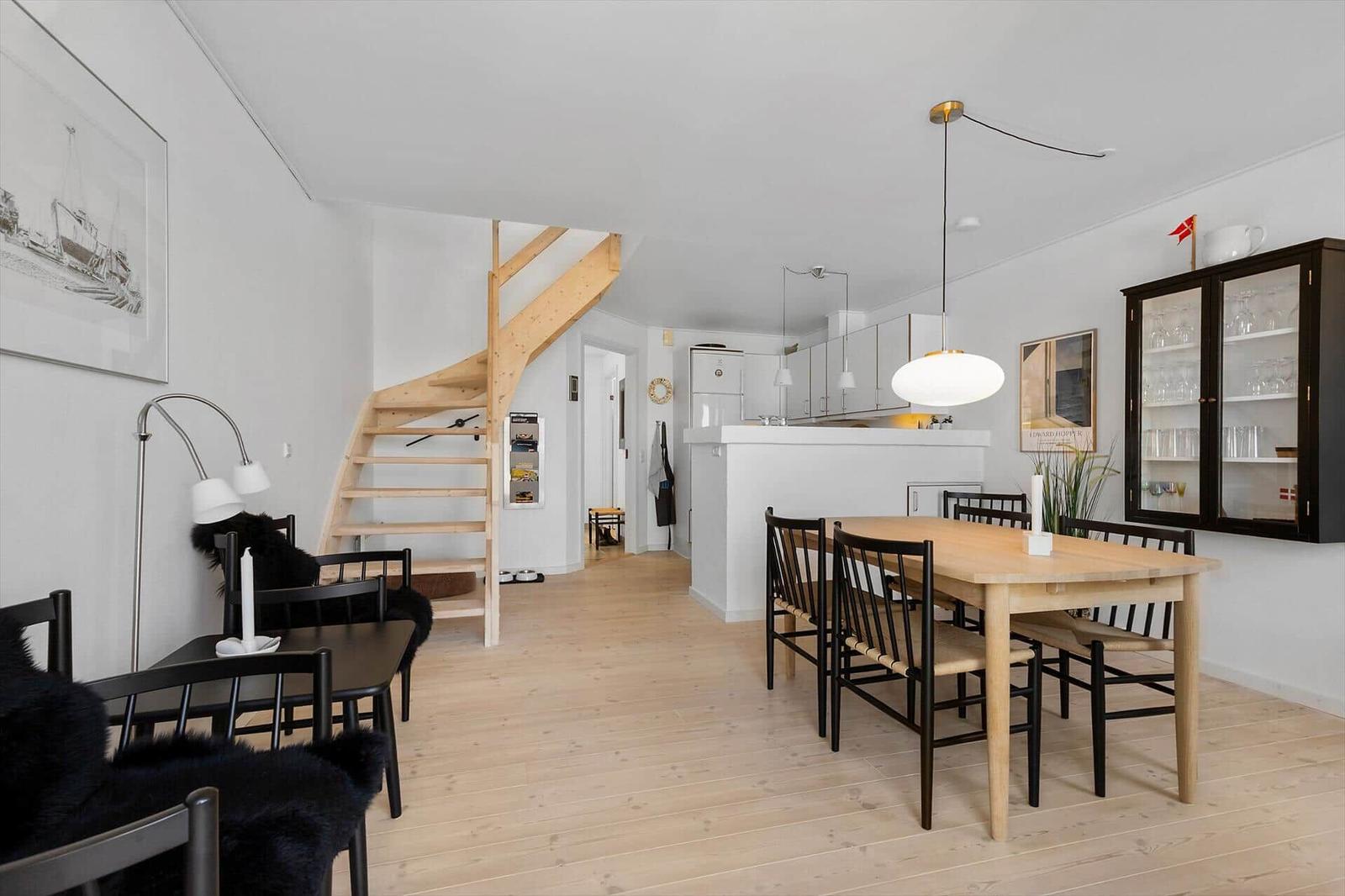 Dining area with wooden table and chairs, adjacent kitchen with island and staircase.