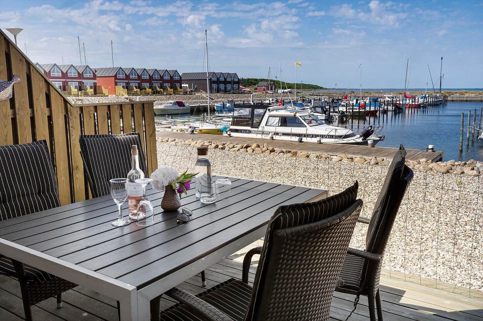 Terrace with table and chairs, view of harbor with boats and houses.