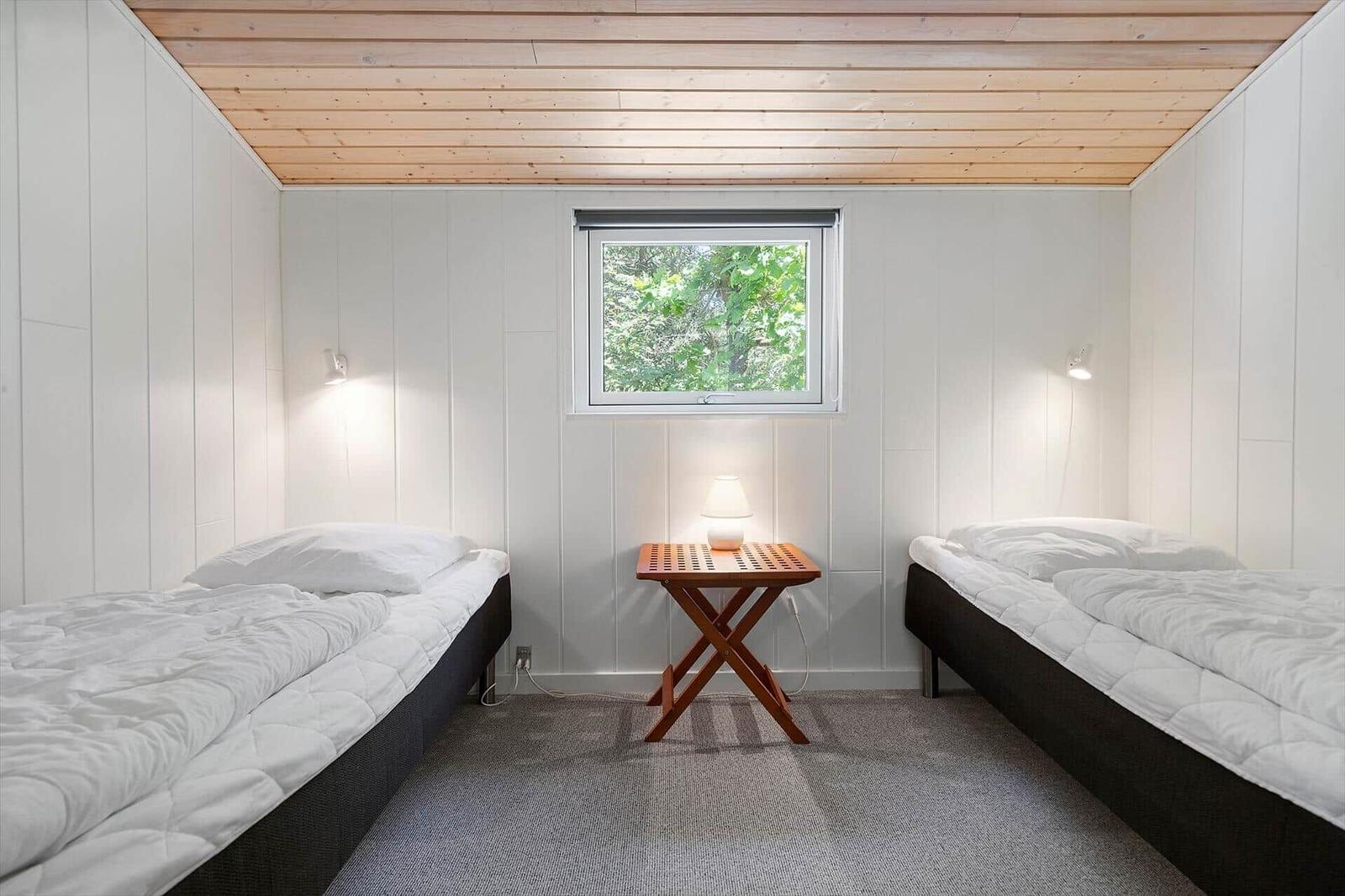 Two beds with white bedding, wooden table, and window with view of trees.