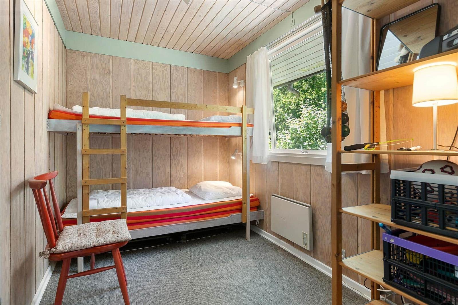 Room with bunk bed, window, and wood paneling.