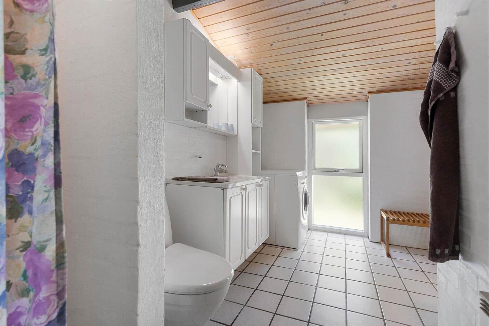 Bathroom with washing machine, toilet, and wooden ceiling.