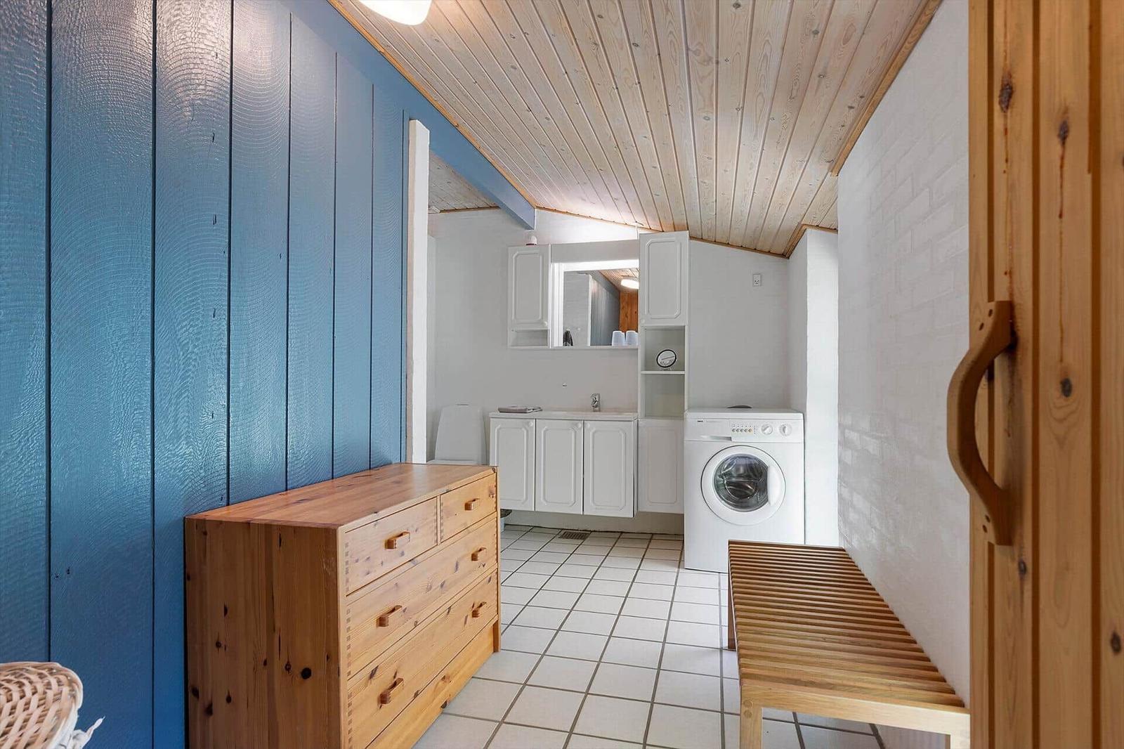 Laundry room with washing machine, cabinets, and wooden furniture. Blue wall and wooden ceiling.