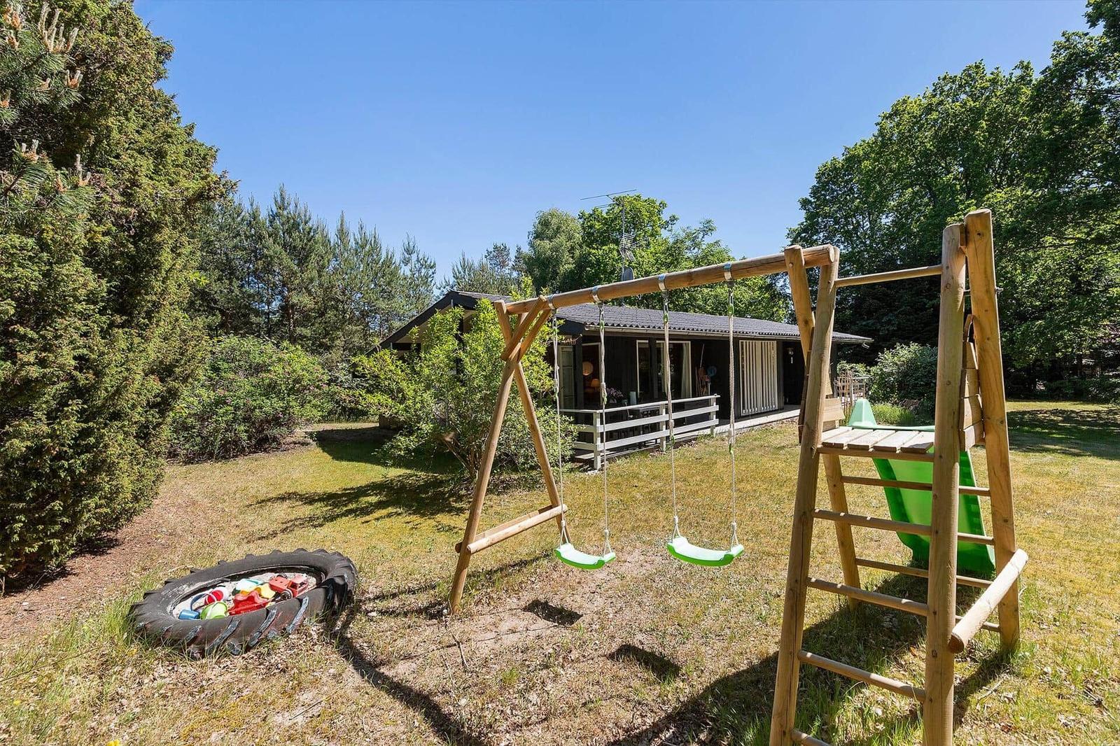 Backyard with playground, swings, and slide. House in background. Lawns and trees.
