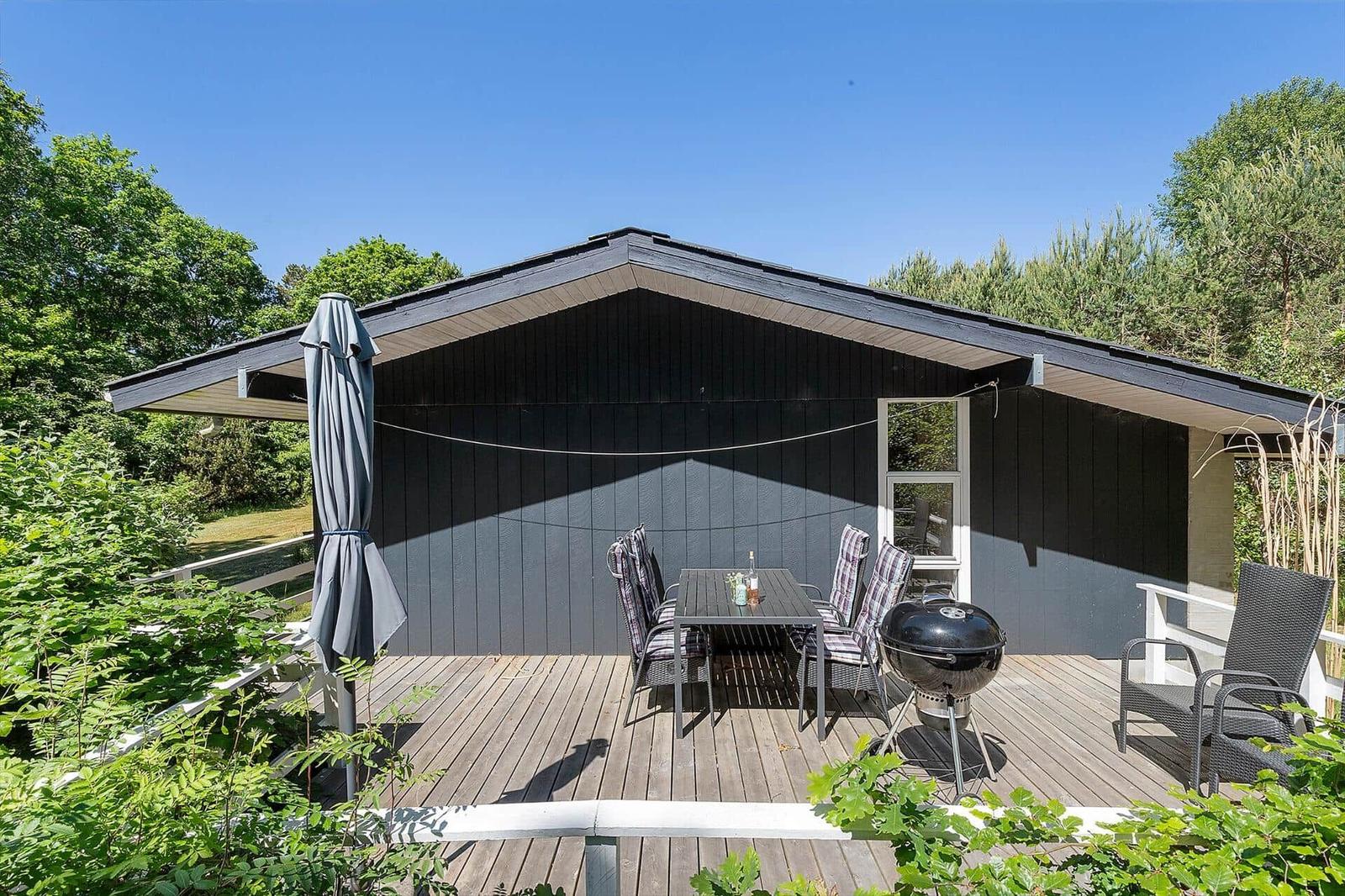 Deck with table, chairs, grill, and umbrella in front of a house.