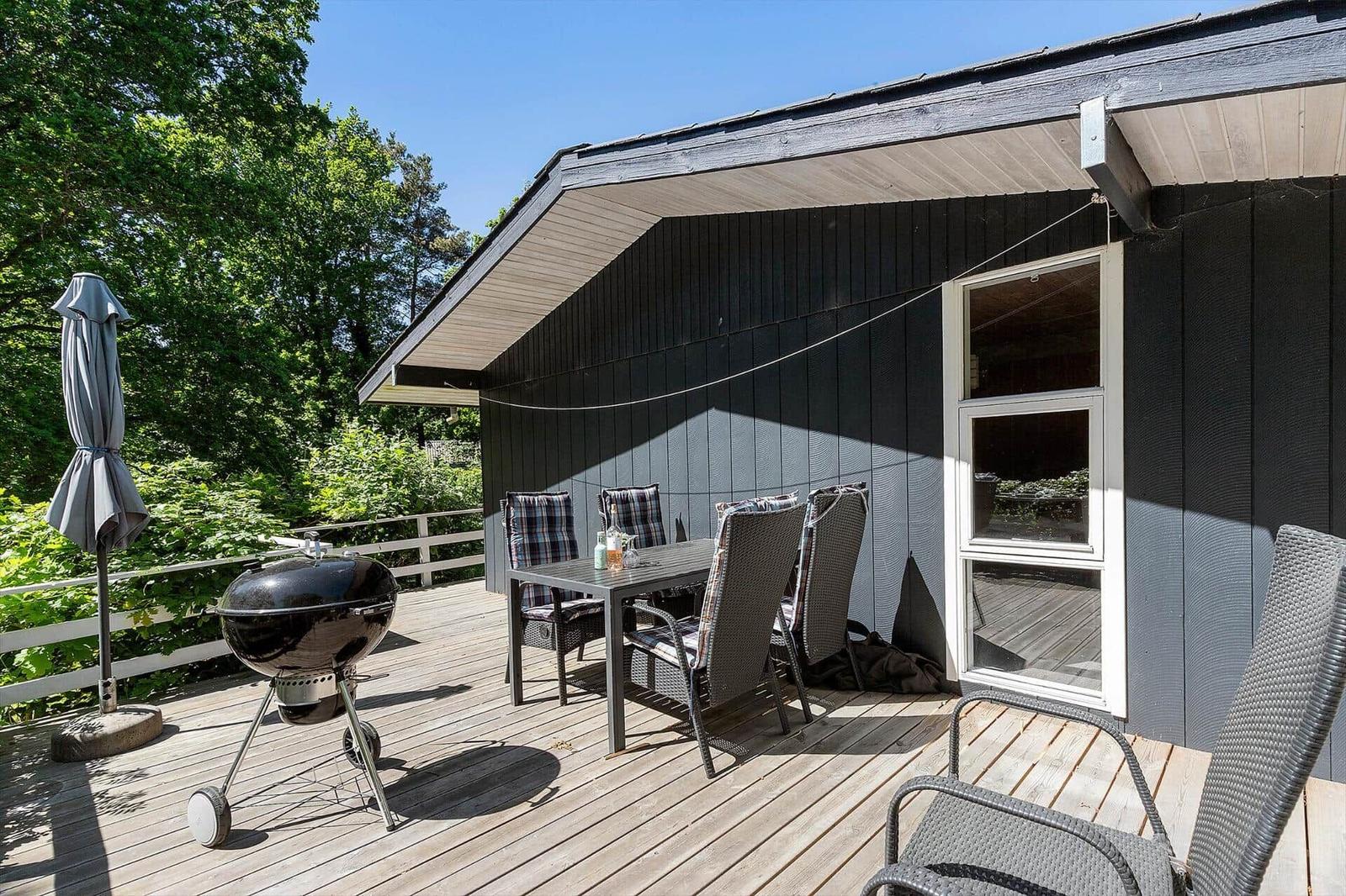 Deck with grill, table, chairs, and umbrella next to a house.