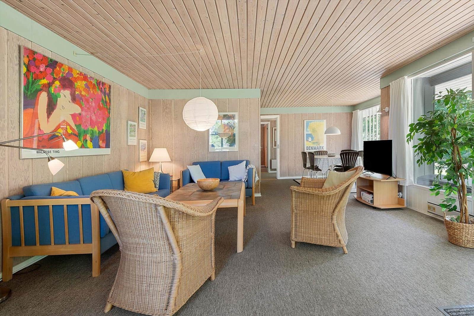 Living room with blue sofa, rattan chairs, and wood ceiling.