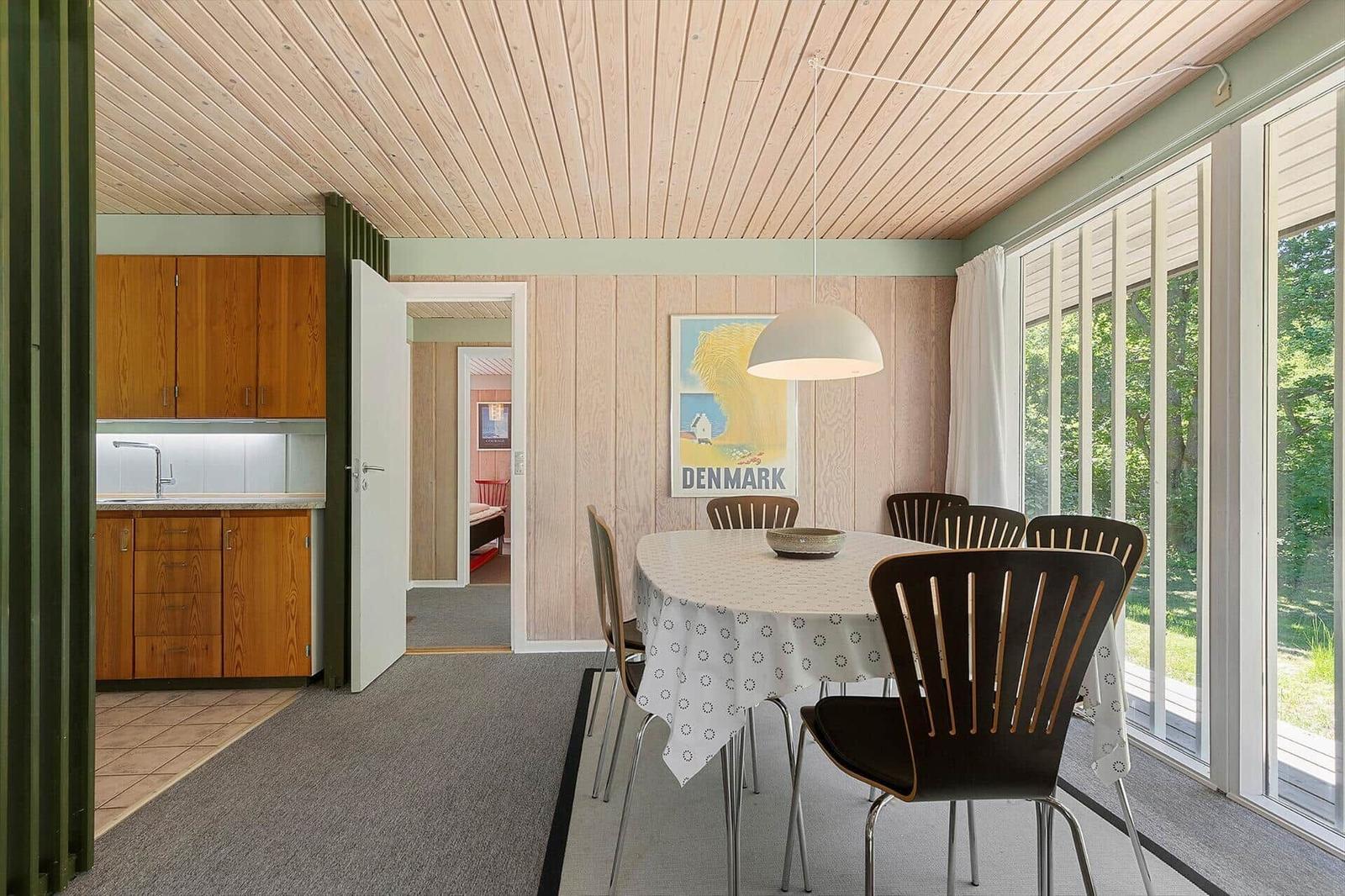 Dining room with table, chairs, and windows. Kitchen and bedroom are visible.