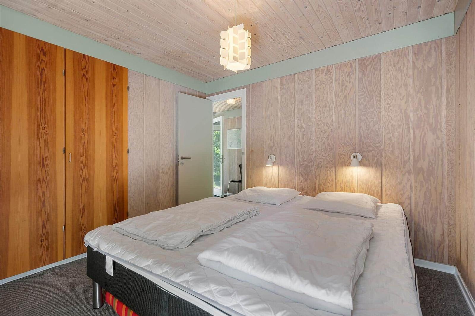 Bedroom with double bed, wood-paneled walls, and ceiling light.