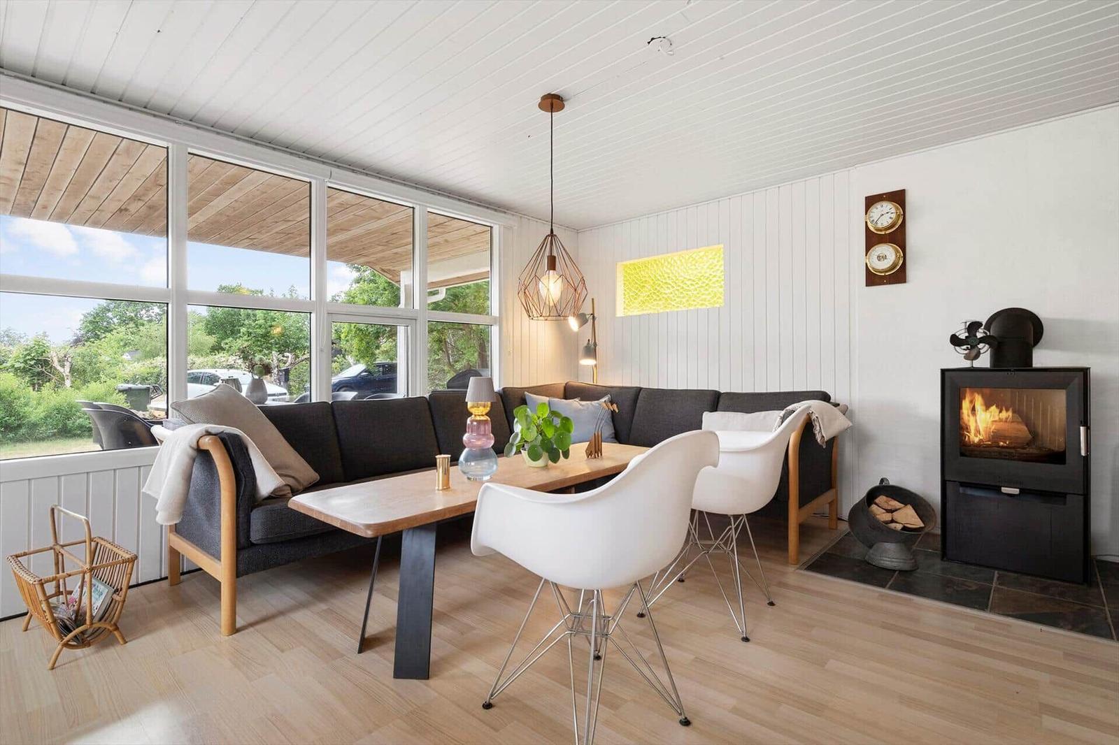 Wohnzimmer mit Sofa, Tisch und Kamin. Große Fenster und Holzboden.