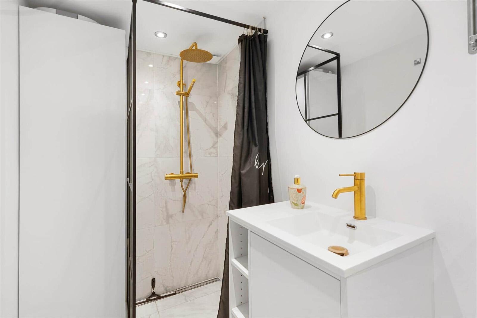 Dusche mit goldener Duschkopf und Waschbecken mit goldener Wasserhahn.
