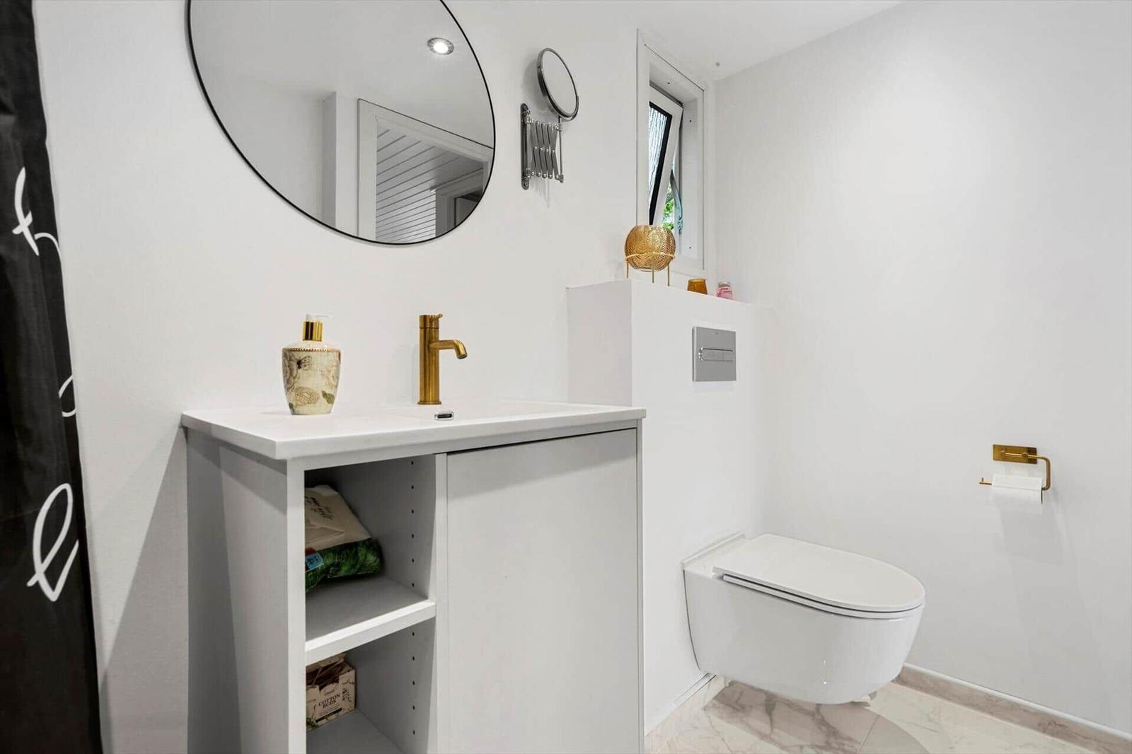 Badezimmer mit Waschbecken, Toilette und Spiegel. Weiße Wände und goldene Armaturen.