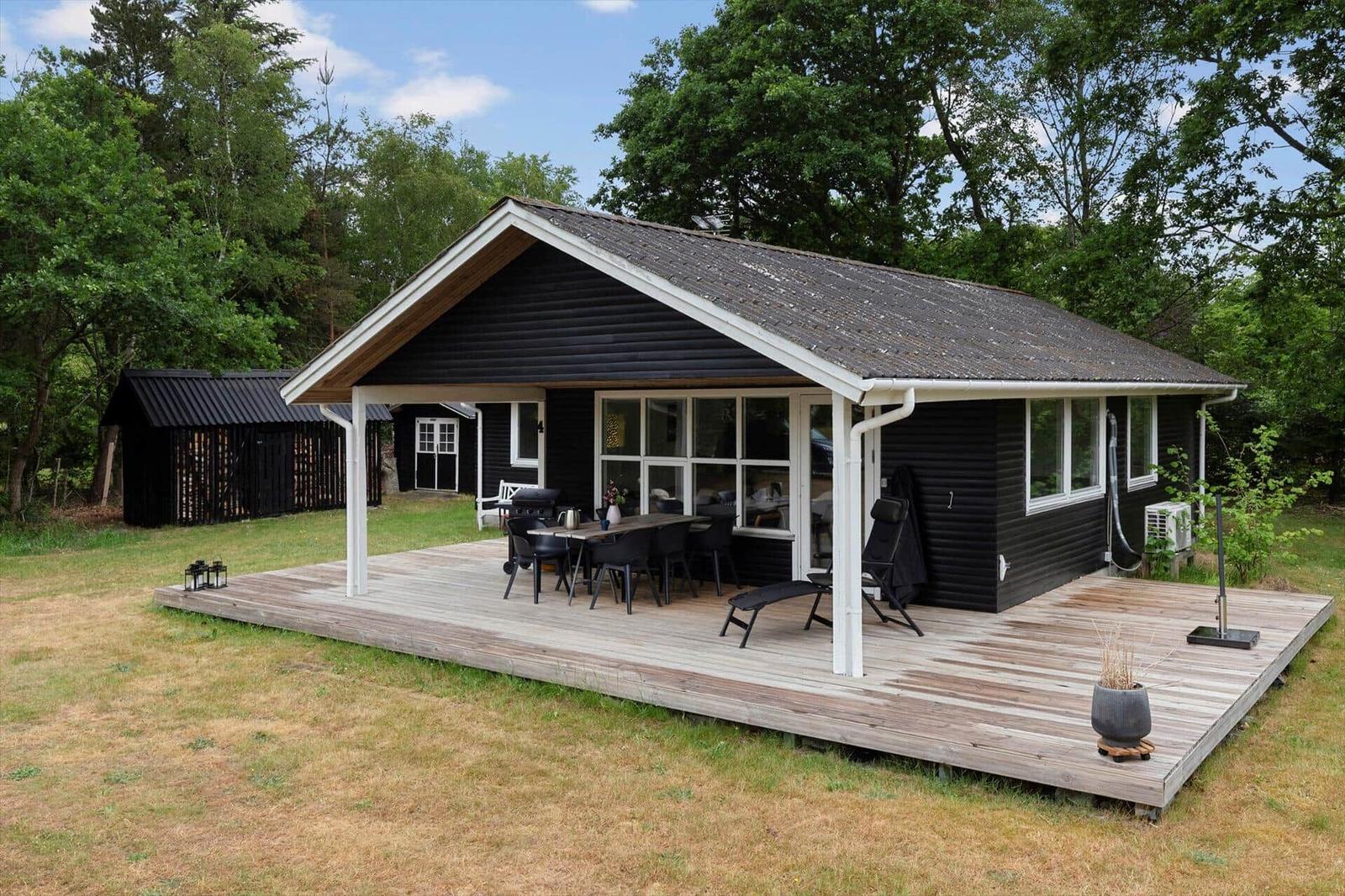 Schwarzes Holzhaus mit Terrasse, Grill und Sitzgelegenheiten im Grünen.