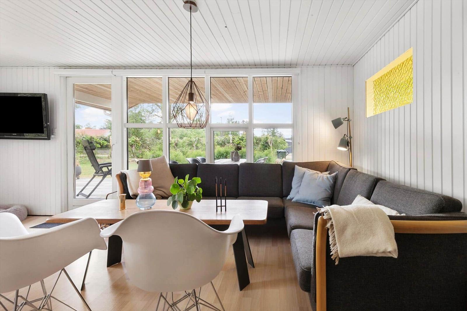 Wohnzimmer mit Ecksofa, Esstisch und großen Fenstern. Holzboden und weiße Wände.