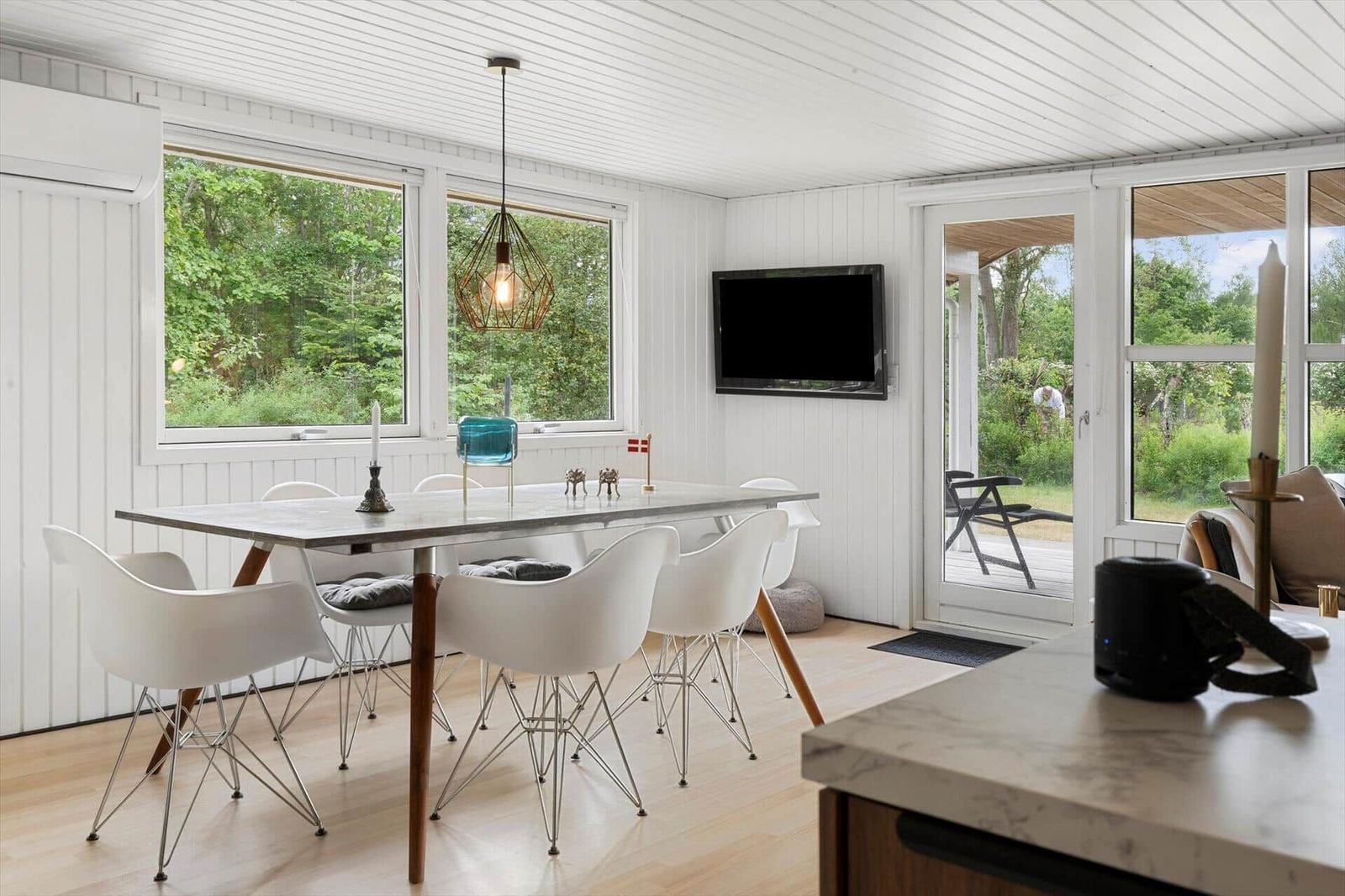 Essbereich mit Tisch, Stühlen und Fernseher. Durchgänge zu Terrasse und Wald.