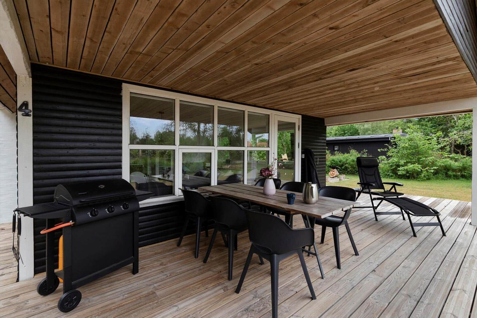 Terrasse mit Grill, Tisch, Stühlen und Liege unter Holzdecke.