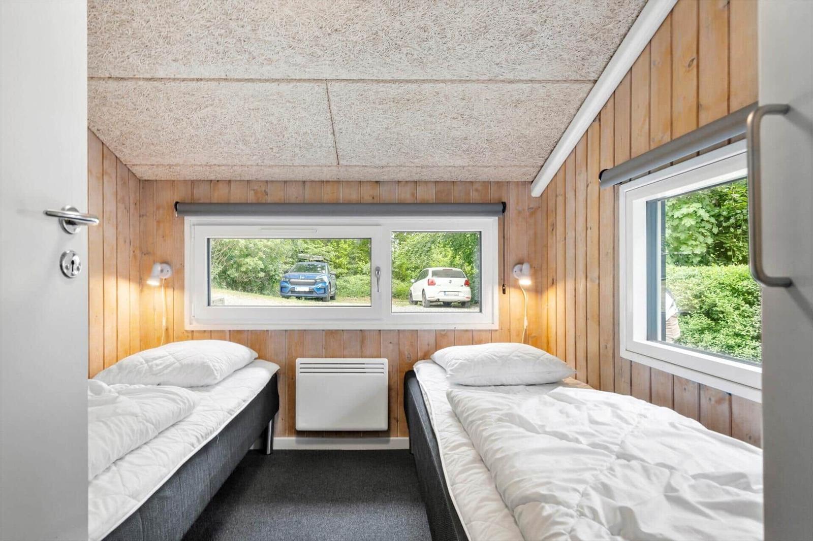 Zwei Betten in einem Raum mit Holzwand und Fenstern. Draußen sind Autos und Bäume sichtbar.