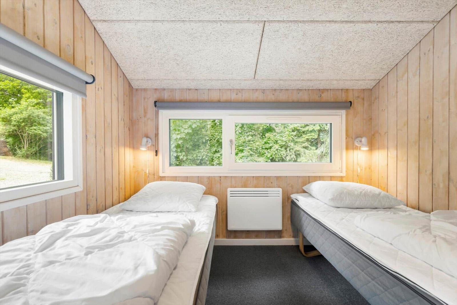 Zwei Betten in einem Zimmer mit Holzwänden und Fenstern zum Wald.