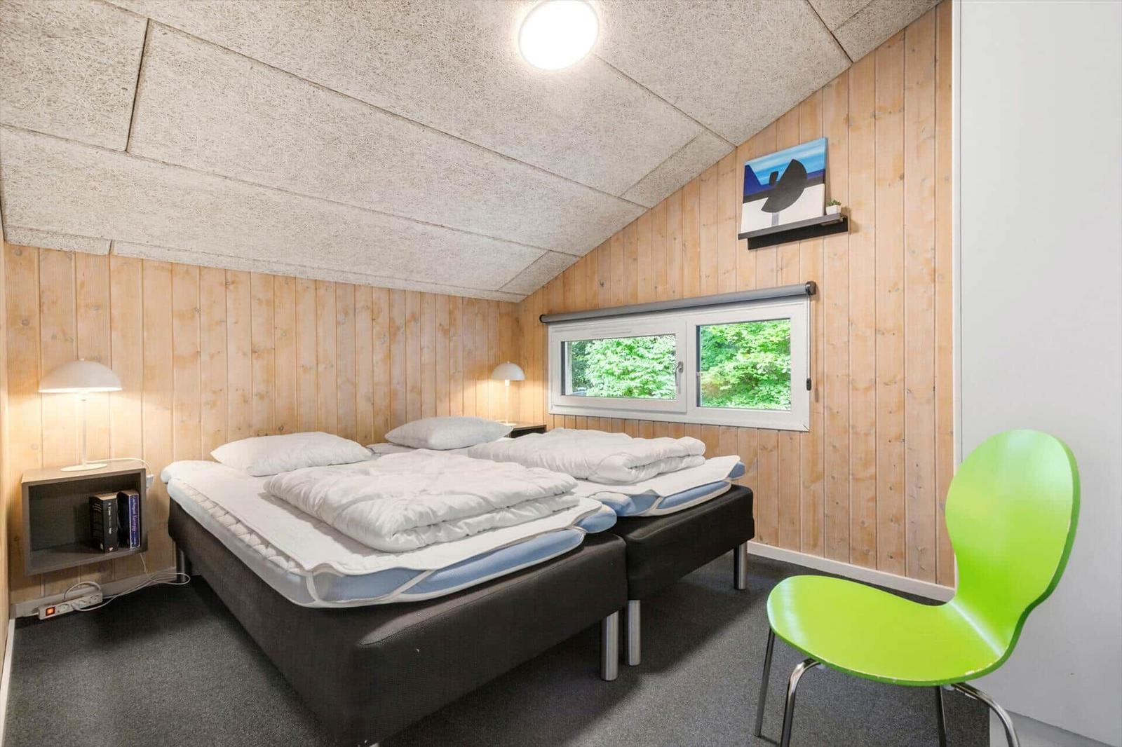 Zimmer mit zwei Betten, grüner Stuhl und Holzwand. Fenster mit Blick auf Grün.