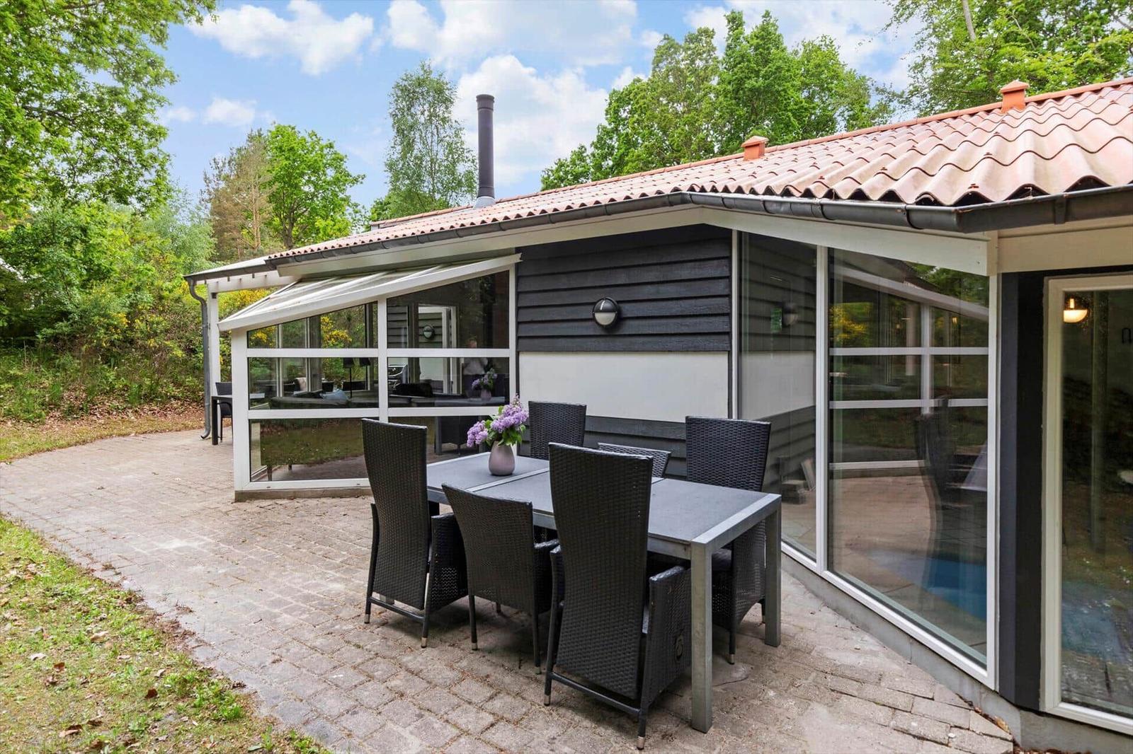 Terrasse mit Tisch und Stühlen vor einem Haus mit Glasfront und Dach