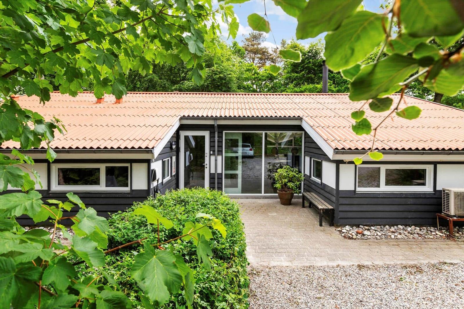 Ein modernes Haus mit Terrasse, Pflanzen und grüner Umgebung.