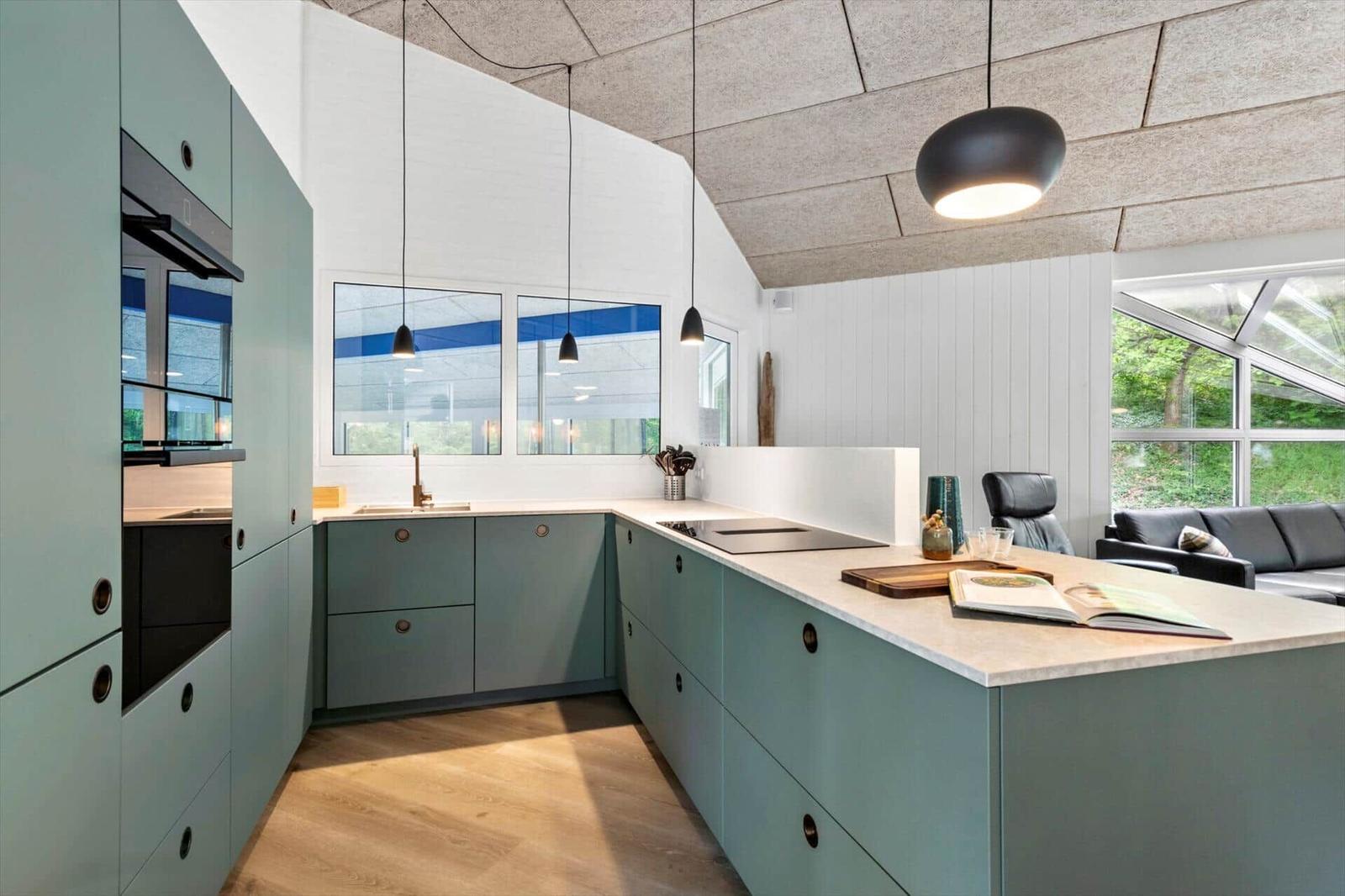 Moderne Küche mit hellblauen Schränken und großem Küchenblock. Blick auf Wohnbereich und Außenbereich.