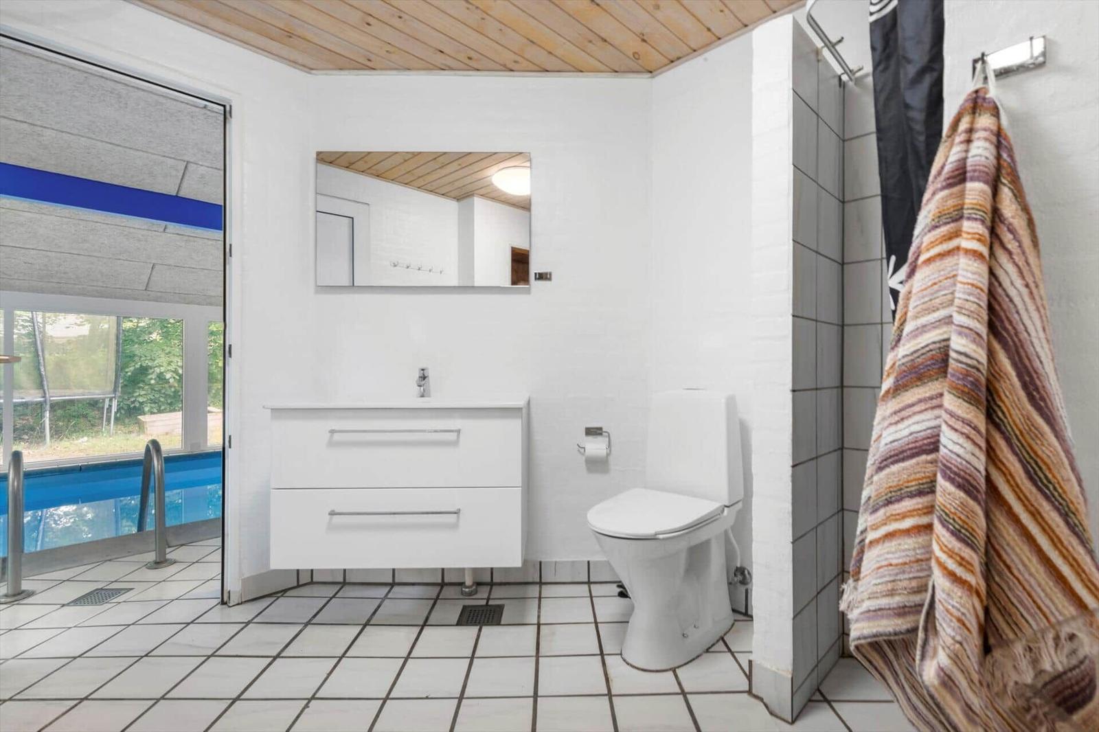 Badezimmer mit Toilette, Waschbecken und Dusche. Blick auf Pool durch Tür.