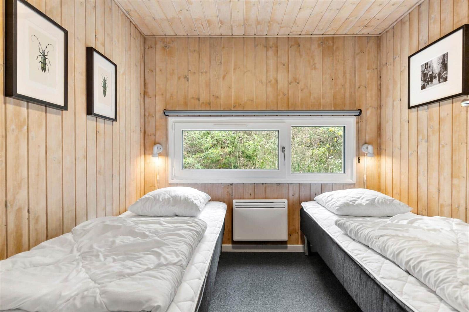 Zwei Einzelbetten mit weißen Bettwäsche, Holzwände und Fenster mit Blick auf Grün.