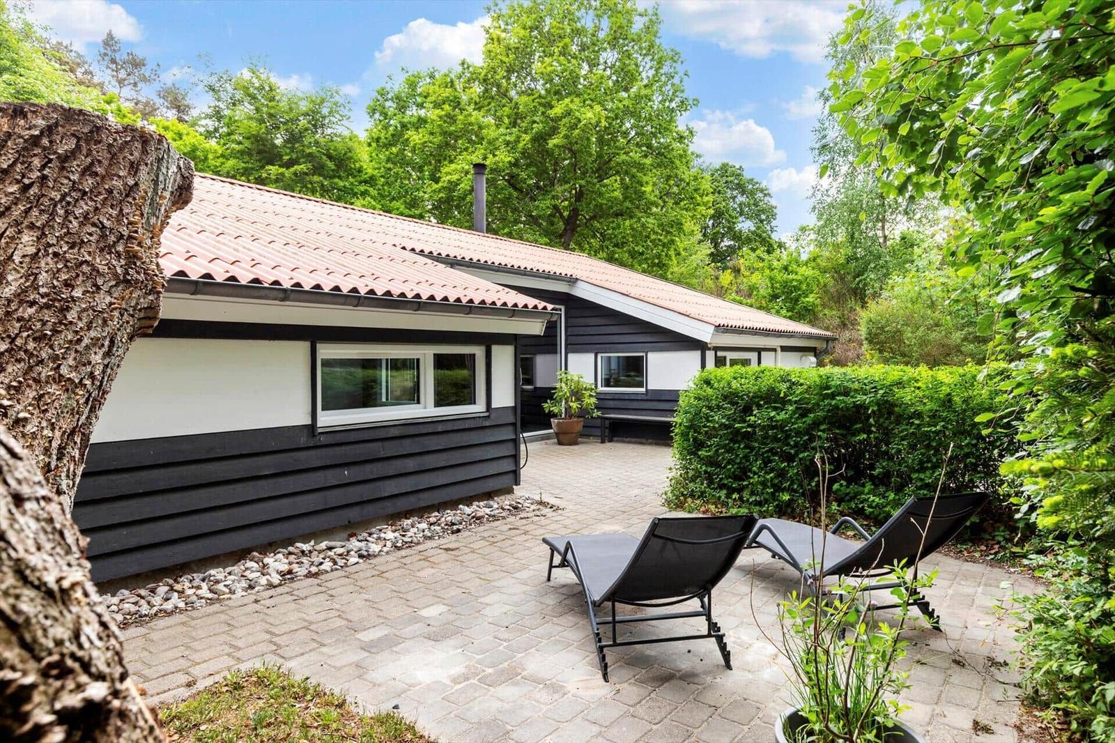 Ein Haus mit Terrasse, Liegestühlen und umgeben von Bäumen und Sträuchern.